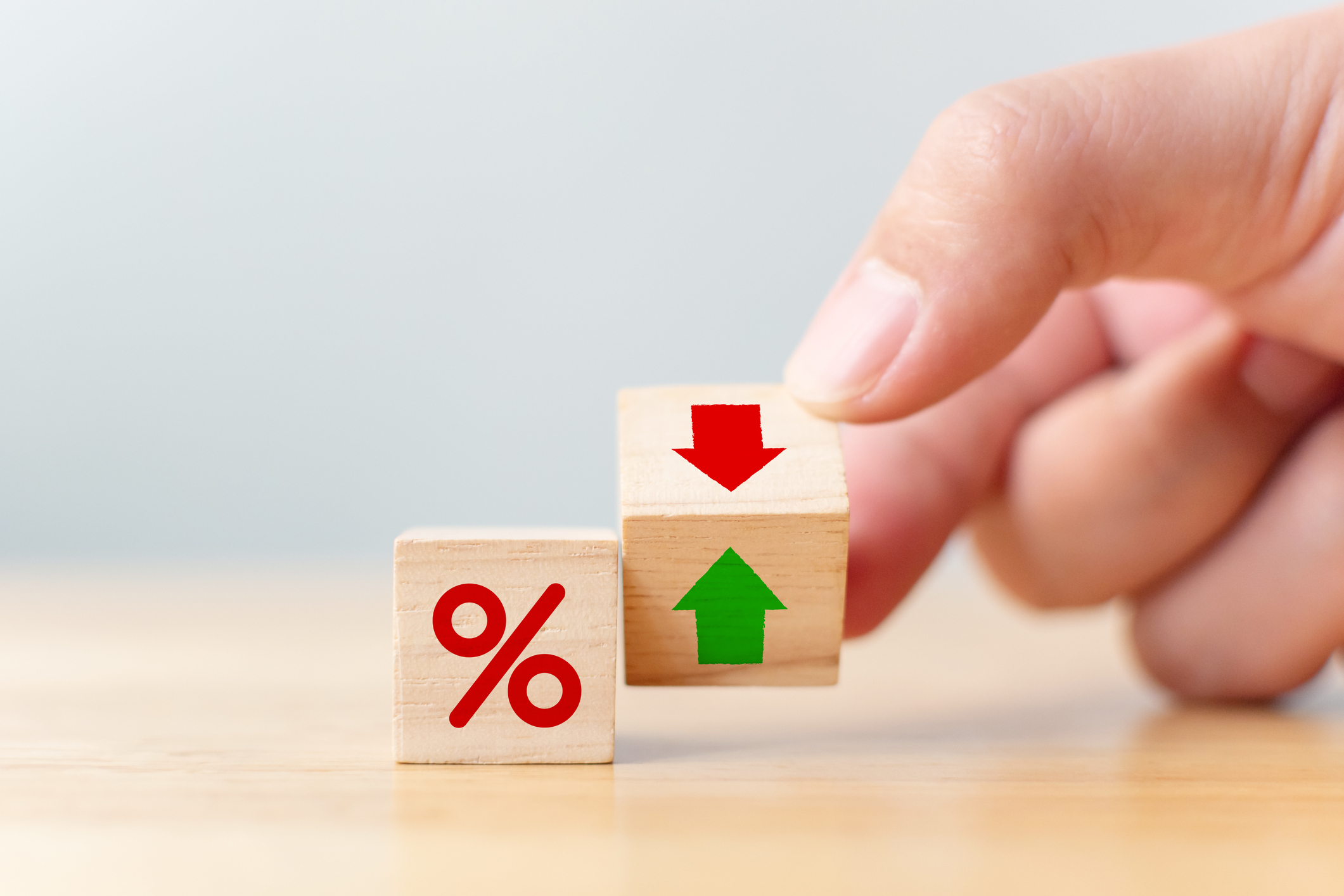 Part of hand holding a cube that is between a down and up arrow next to a percentage sign.