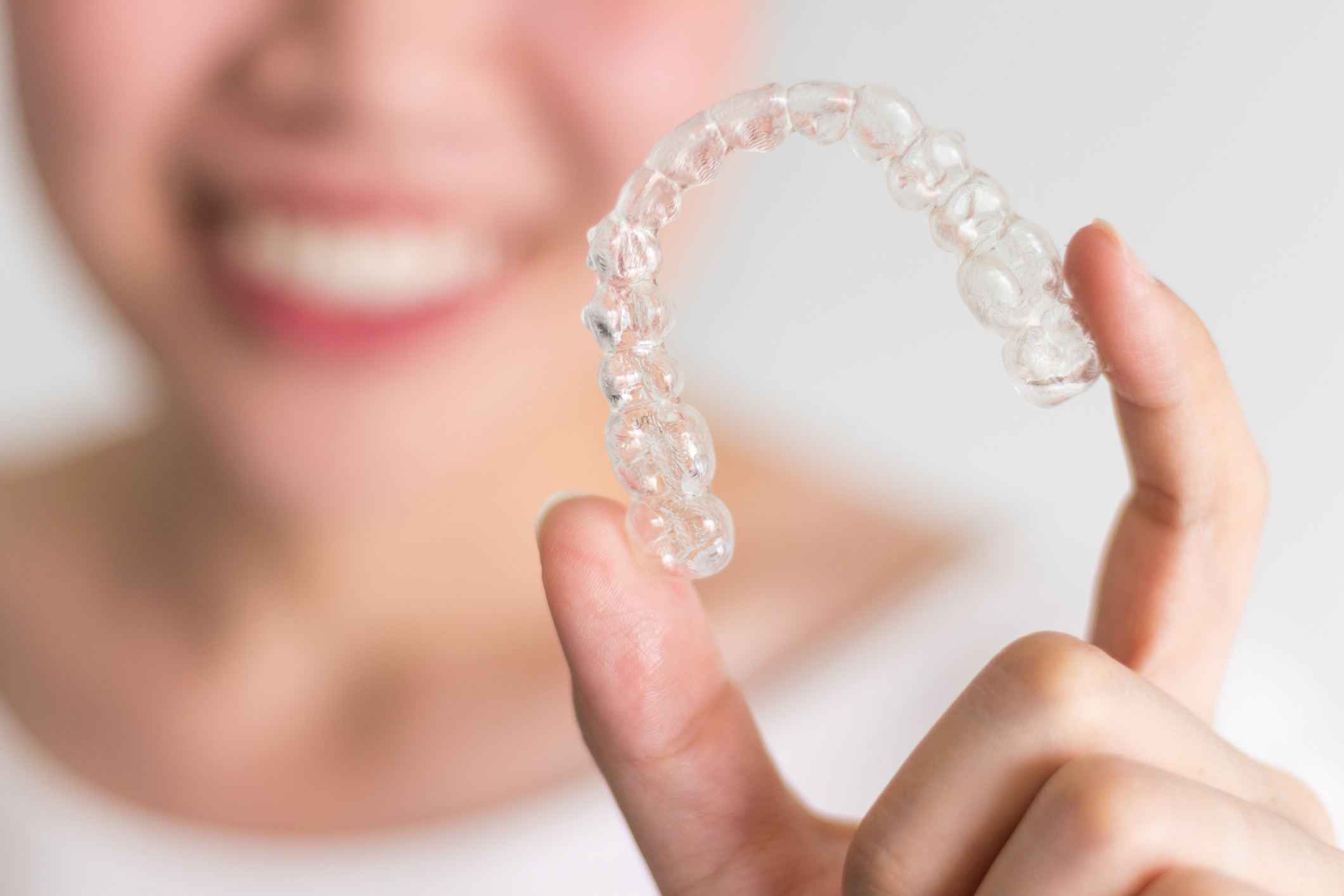 Smiling woman holding a clear orthodontic aligner