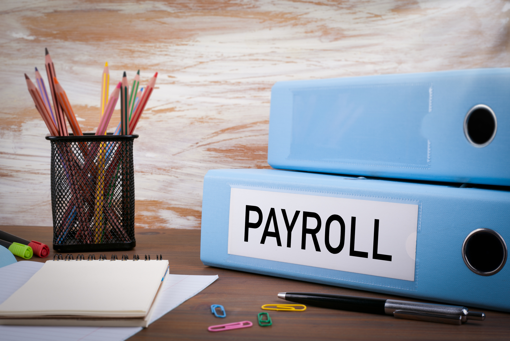 Blue binder labeled payroll on a table with office supplies