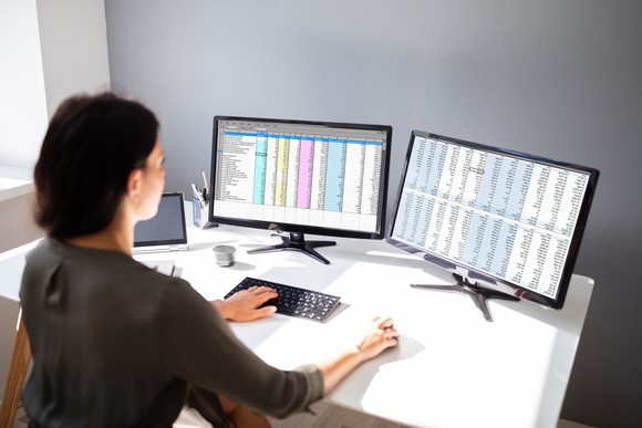 A woman works on a database across two monitors.