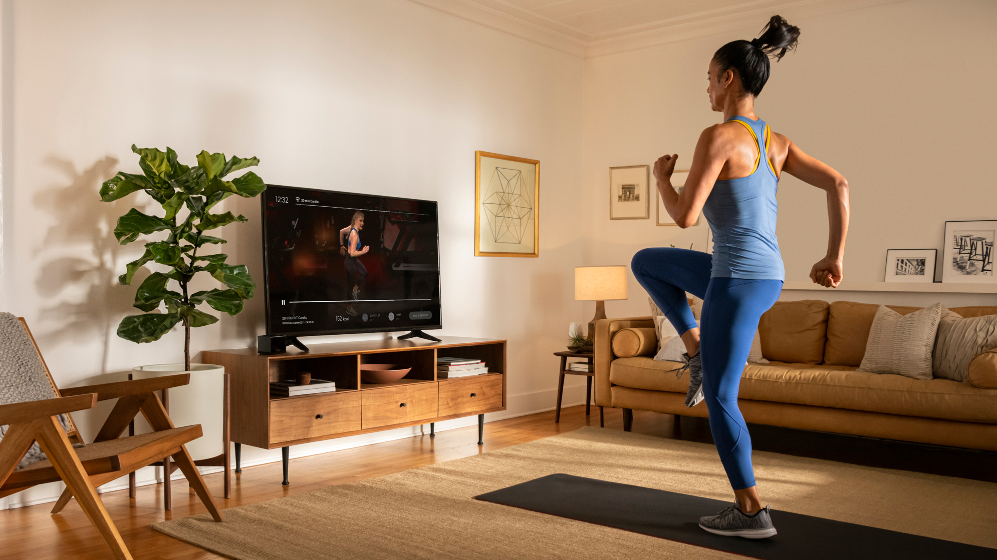 A younger woman follows a Peloton online class to work out in her living room.