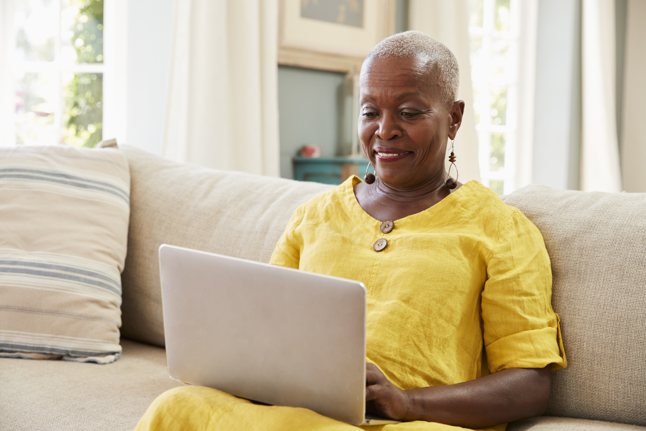 Smiling older woman sitting on couch with laptop in lap