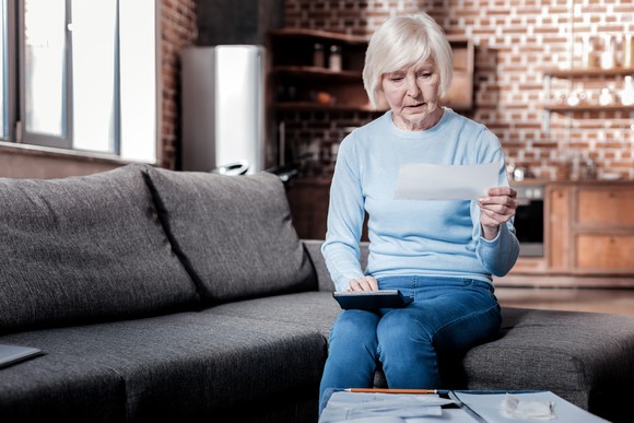 Older woman sitting on couch with calculator and financial documents.