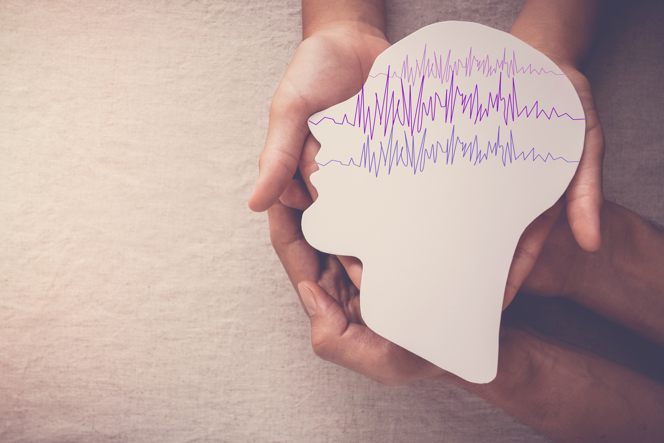 Hands holding cutout of head with brain waves