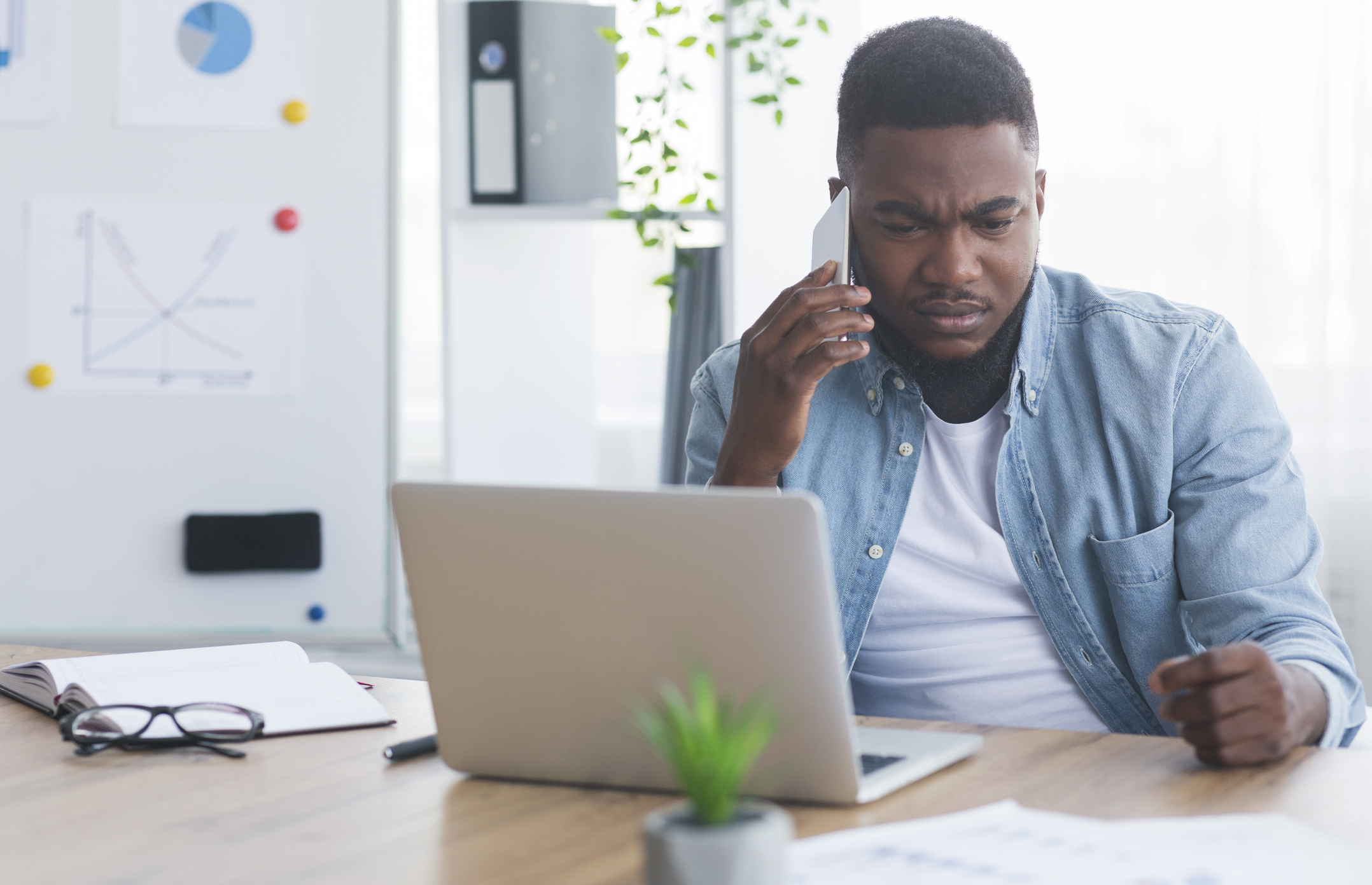 A person on their cellphone sitting in front of a laptop.