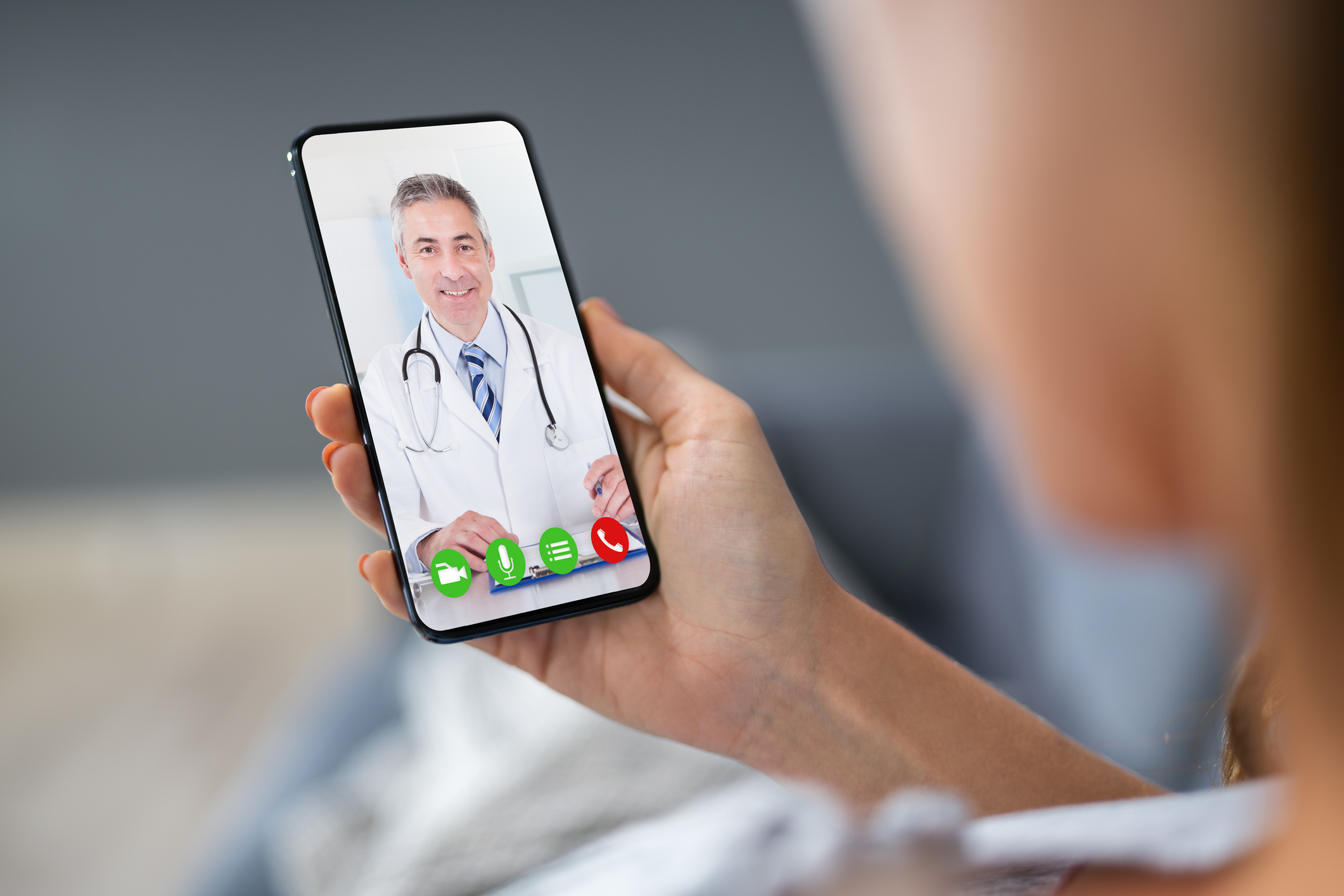 Person holding a smartphone displaying a video call with a doctor.