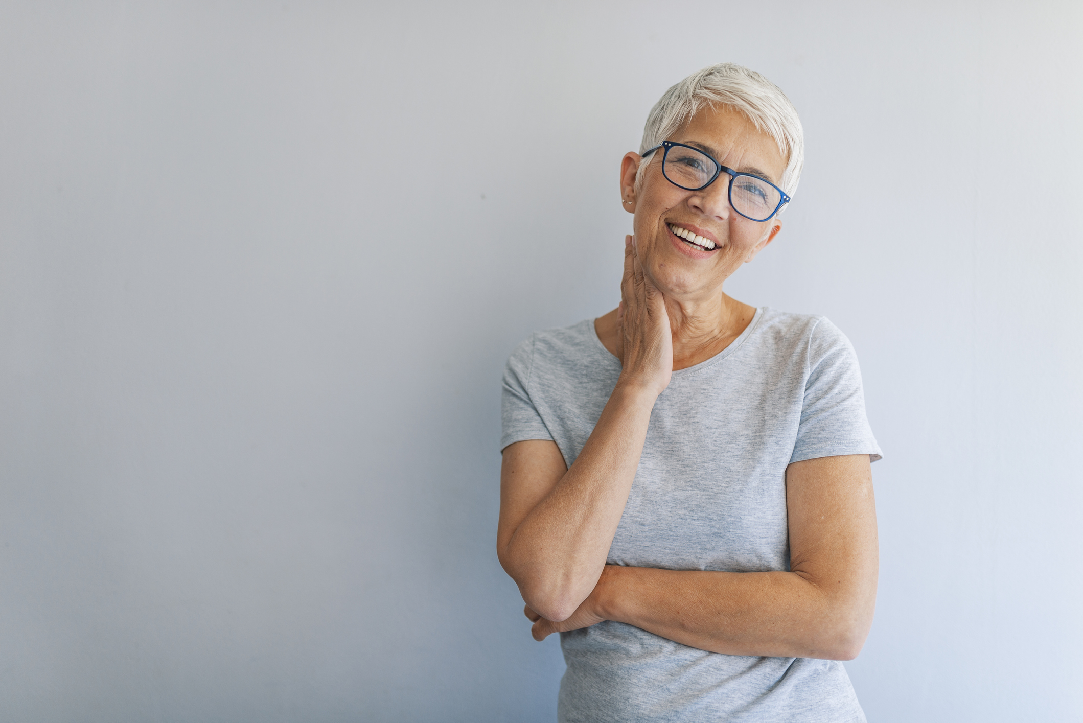 Smiling older woman standing against gray wall