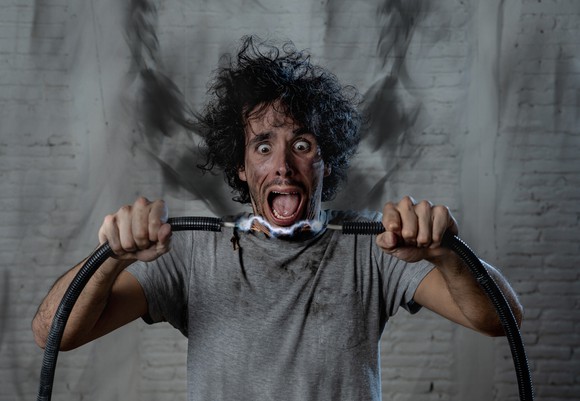 A man covered in scorch marks holds together two electric cables.