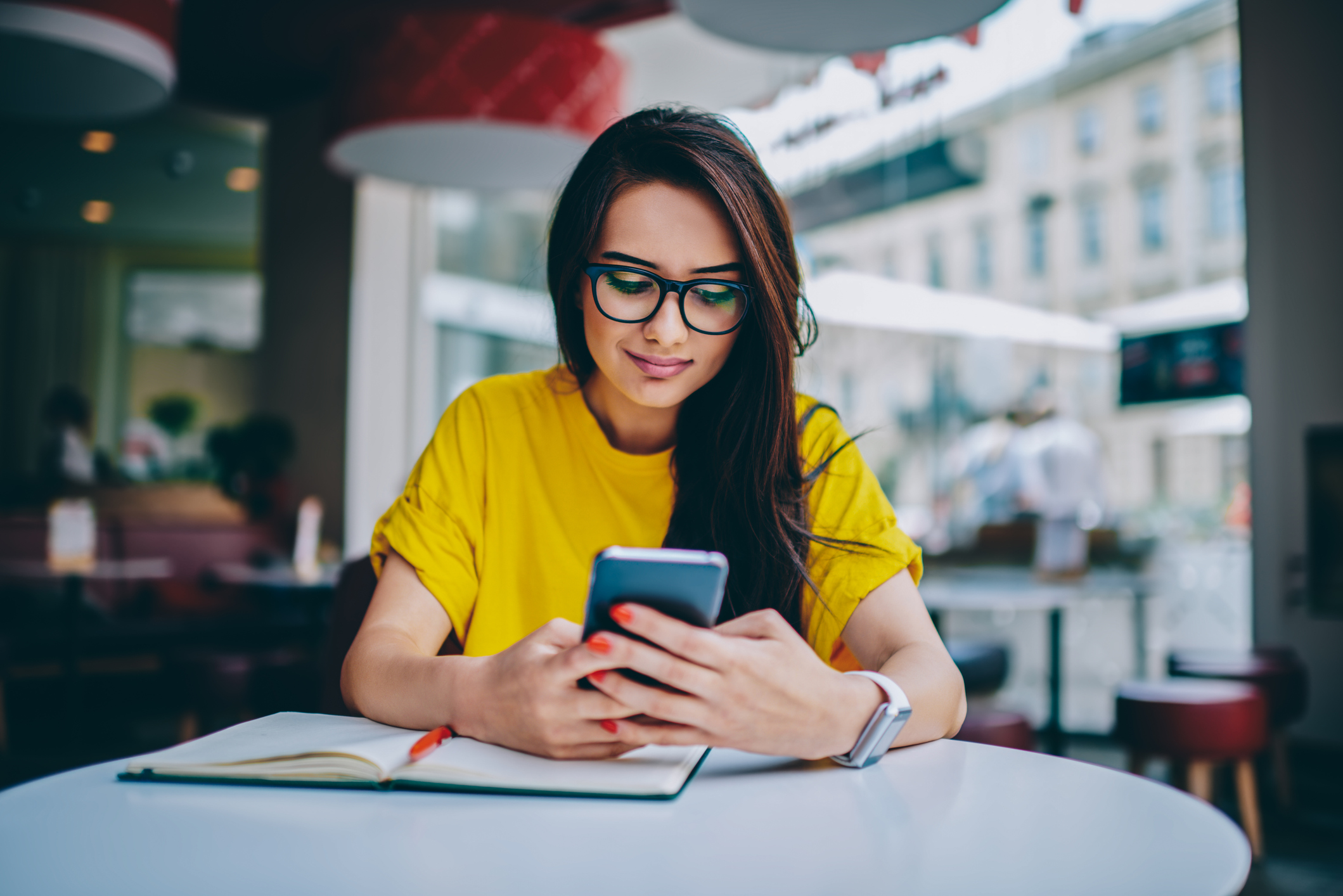 A woman uses her smartphone at a table with an open notebook