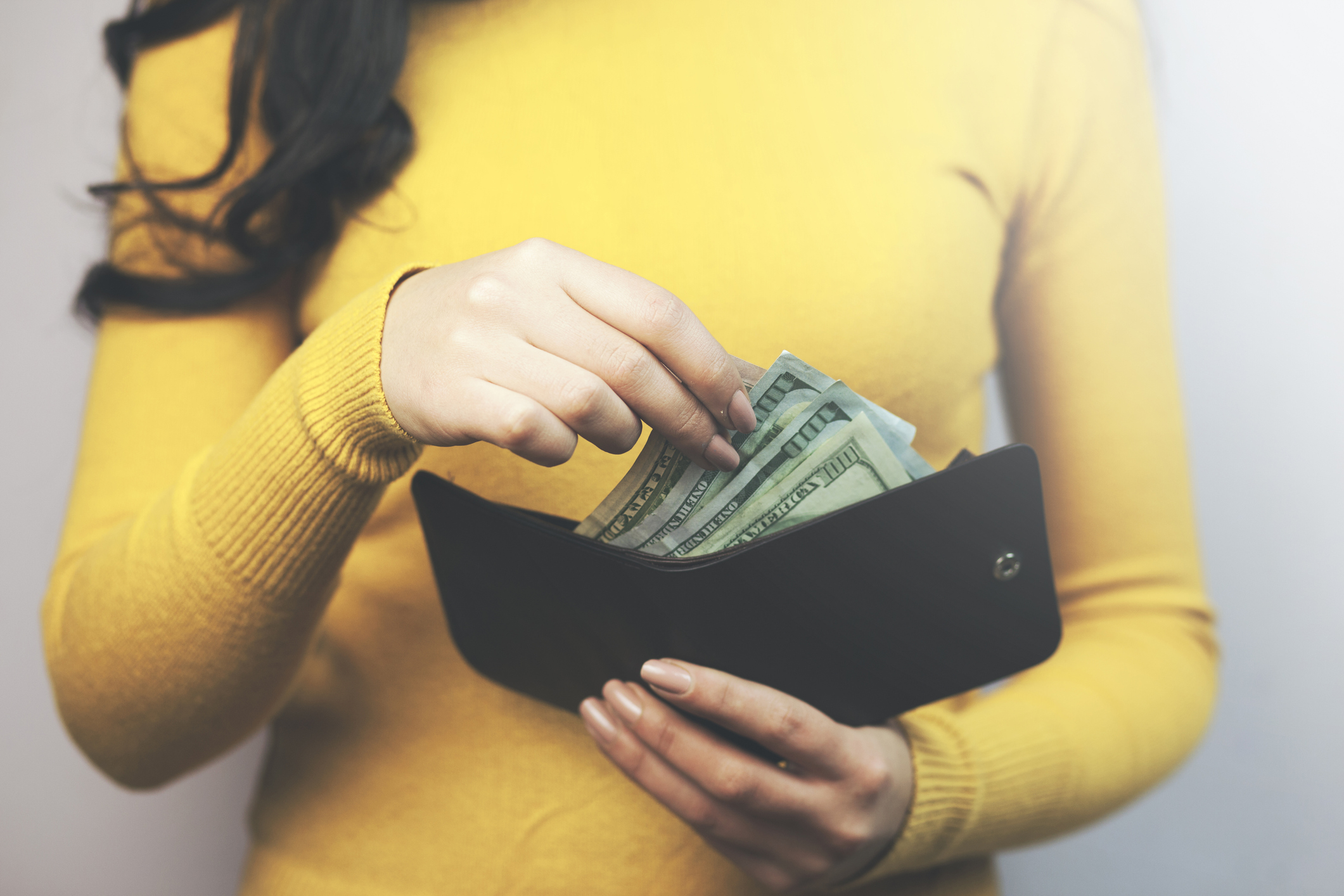 A woman reaches into her wallet filled with $100 bills.