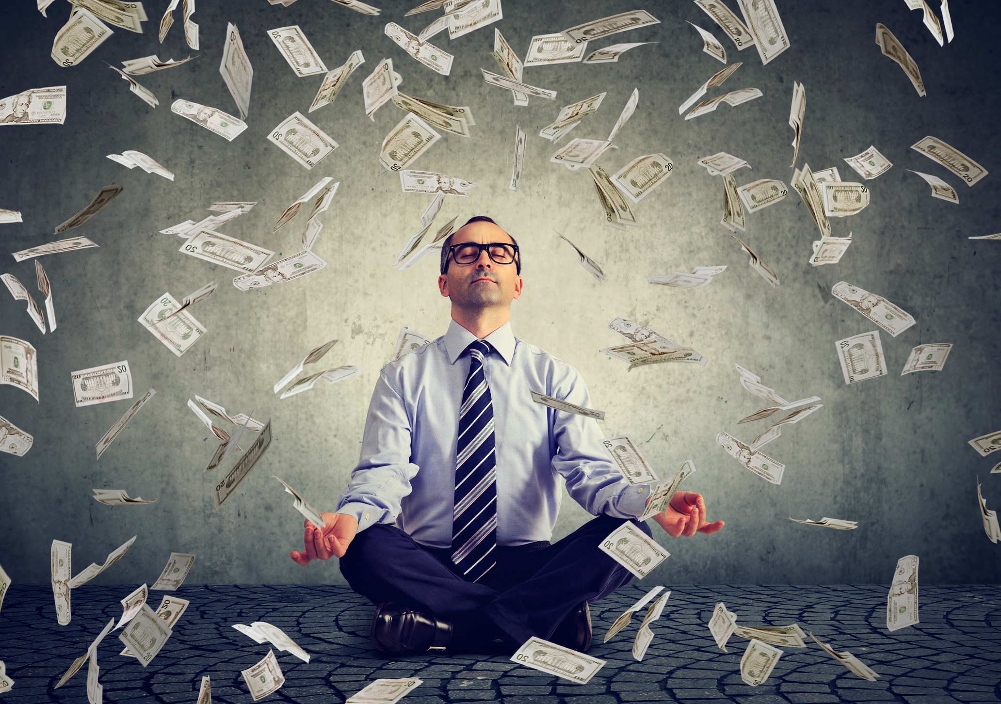Man in meditation with money falling down around him.