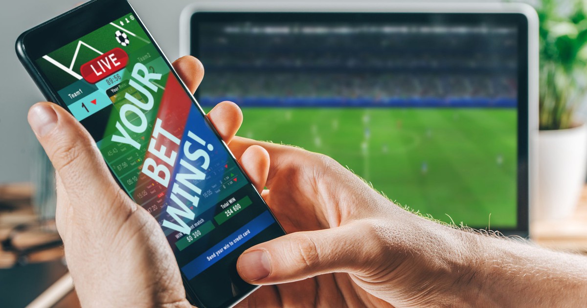 Smartphone with screen saying Your Bet Wins next to computer showing soccer game.