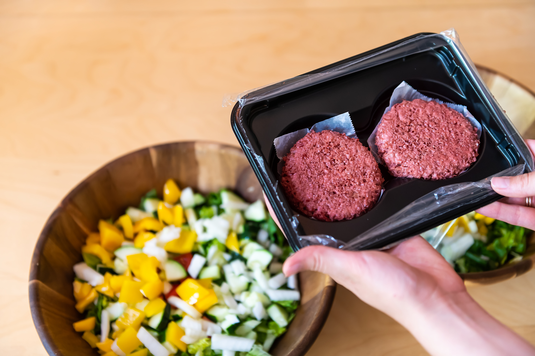 Hands hold a package of two plant-based meat patties over a salad bowl.