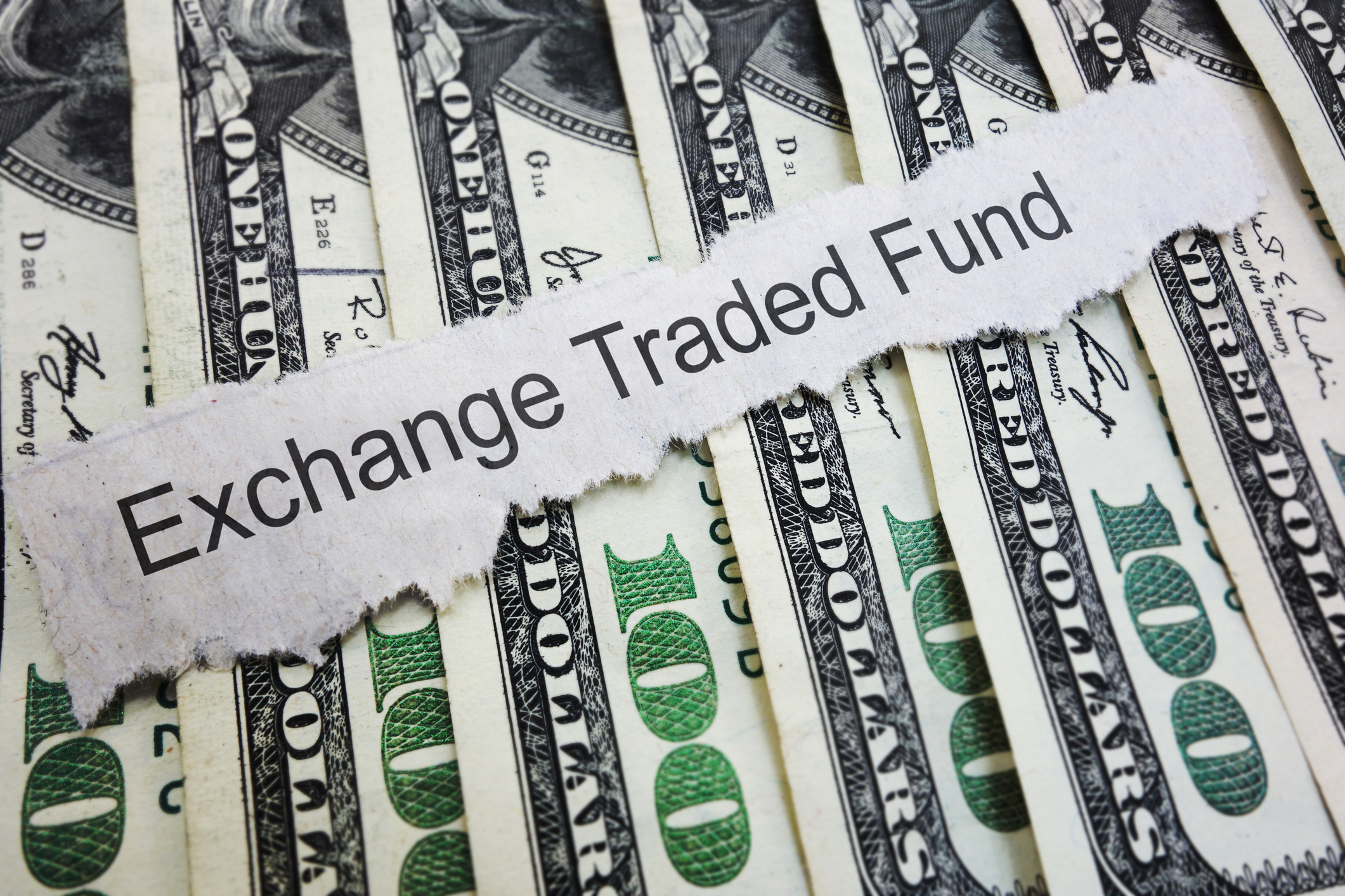 "Exchange Traded Fund" printed on a slip of paper laid atop a stack of $100 bills.