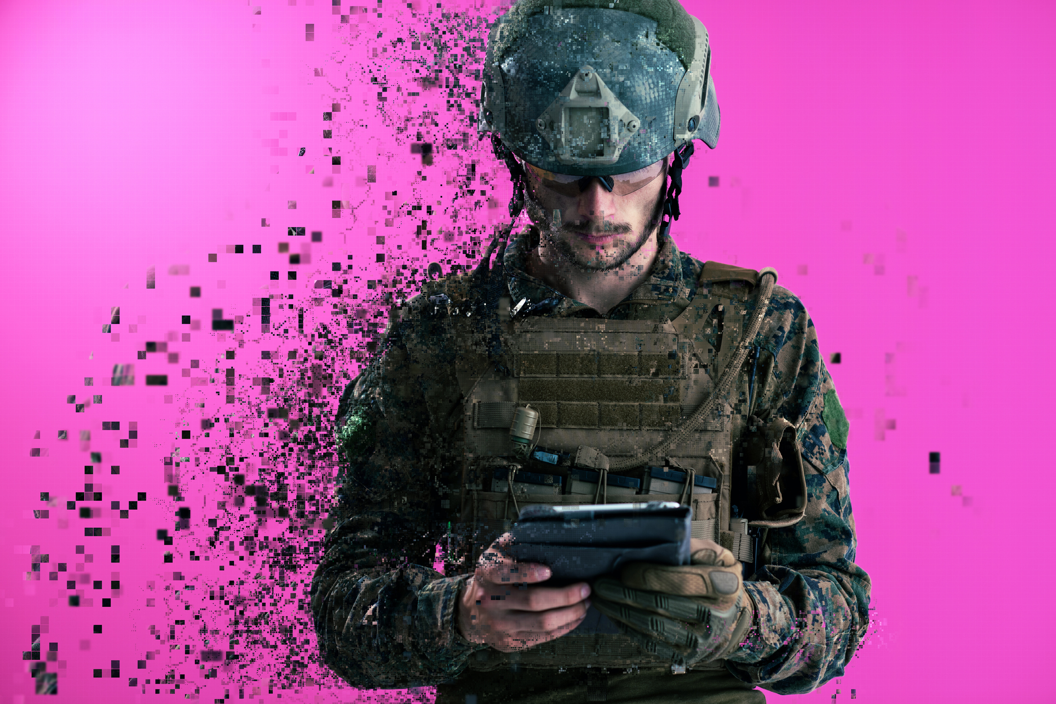A soldier in fatigues holds a tablet against a magenta background.