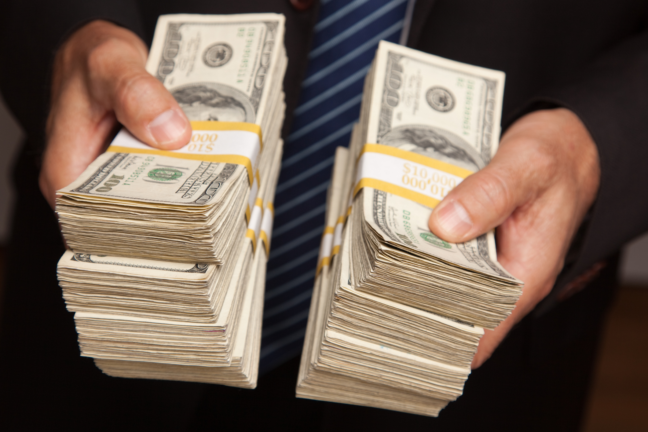 A businessman handing over stacks of one hundred dollar bills.