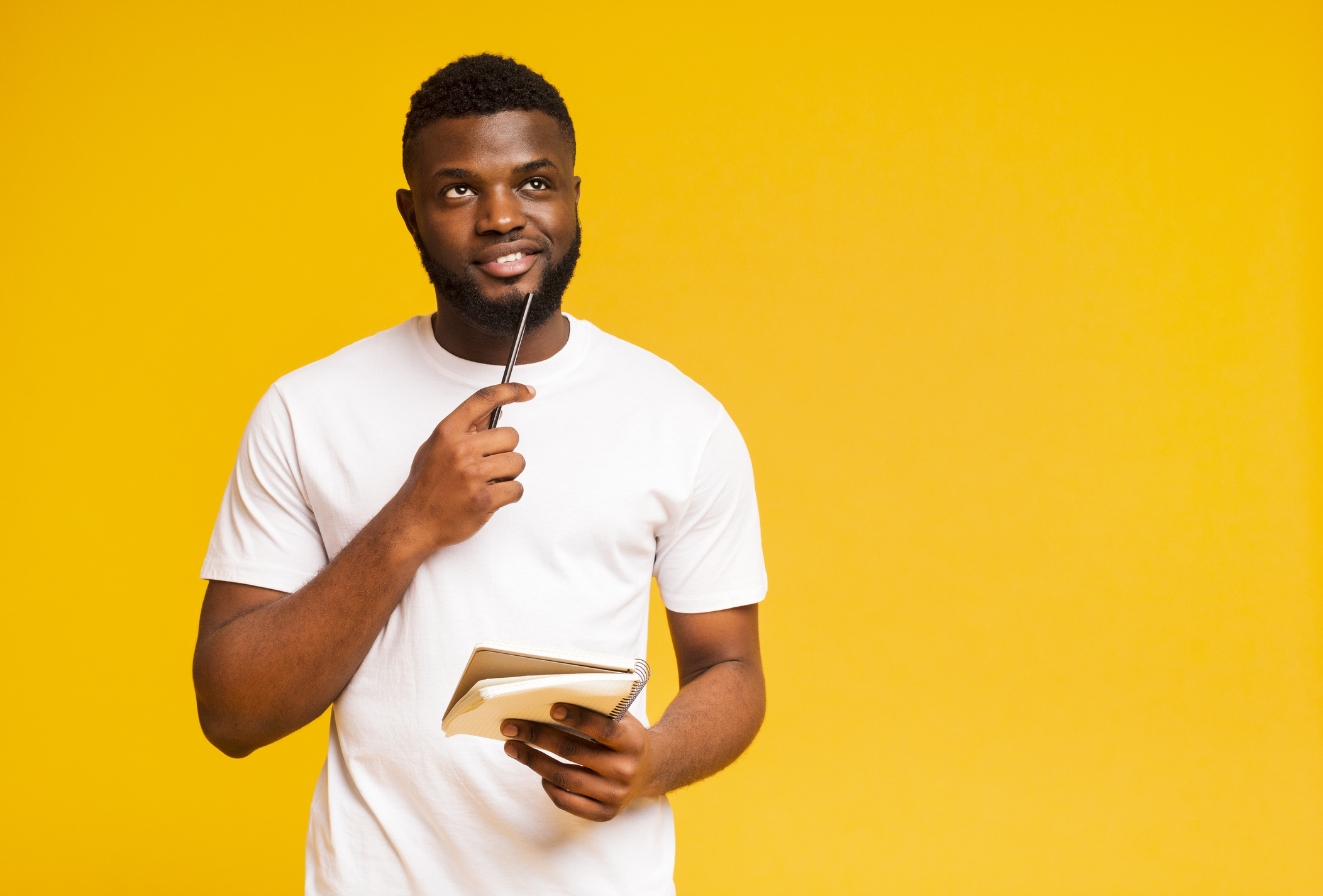 A man thinks while holding a pad of paper and a pencil.
