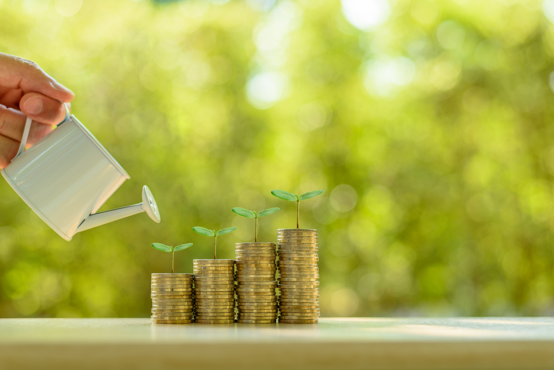 Person watering ascending stacks of coins with little plants growing from them.