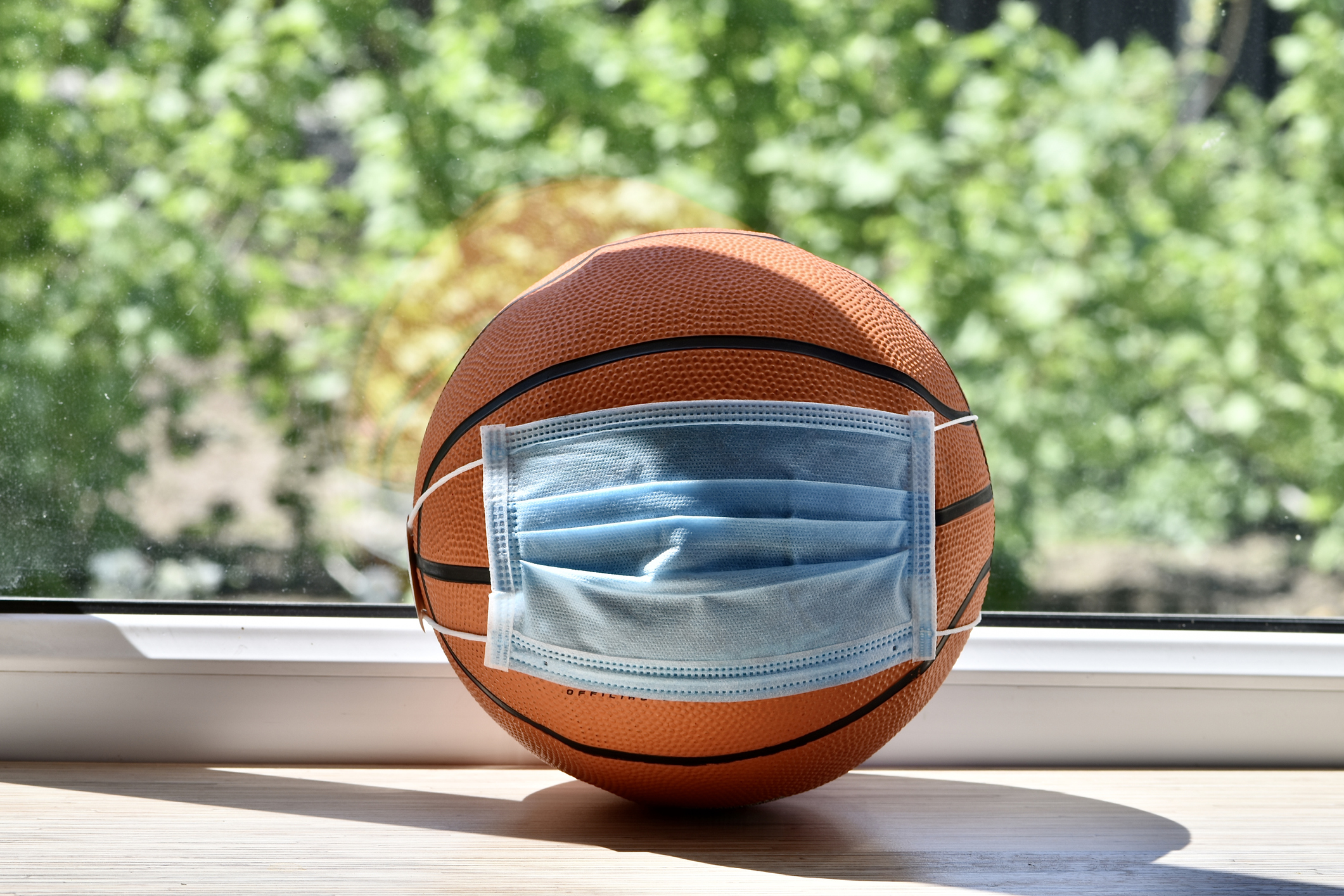 A basketball wearing a blue mask, on a tablein front of a window