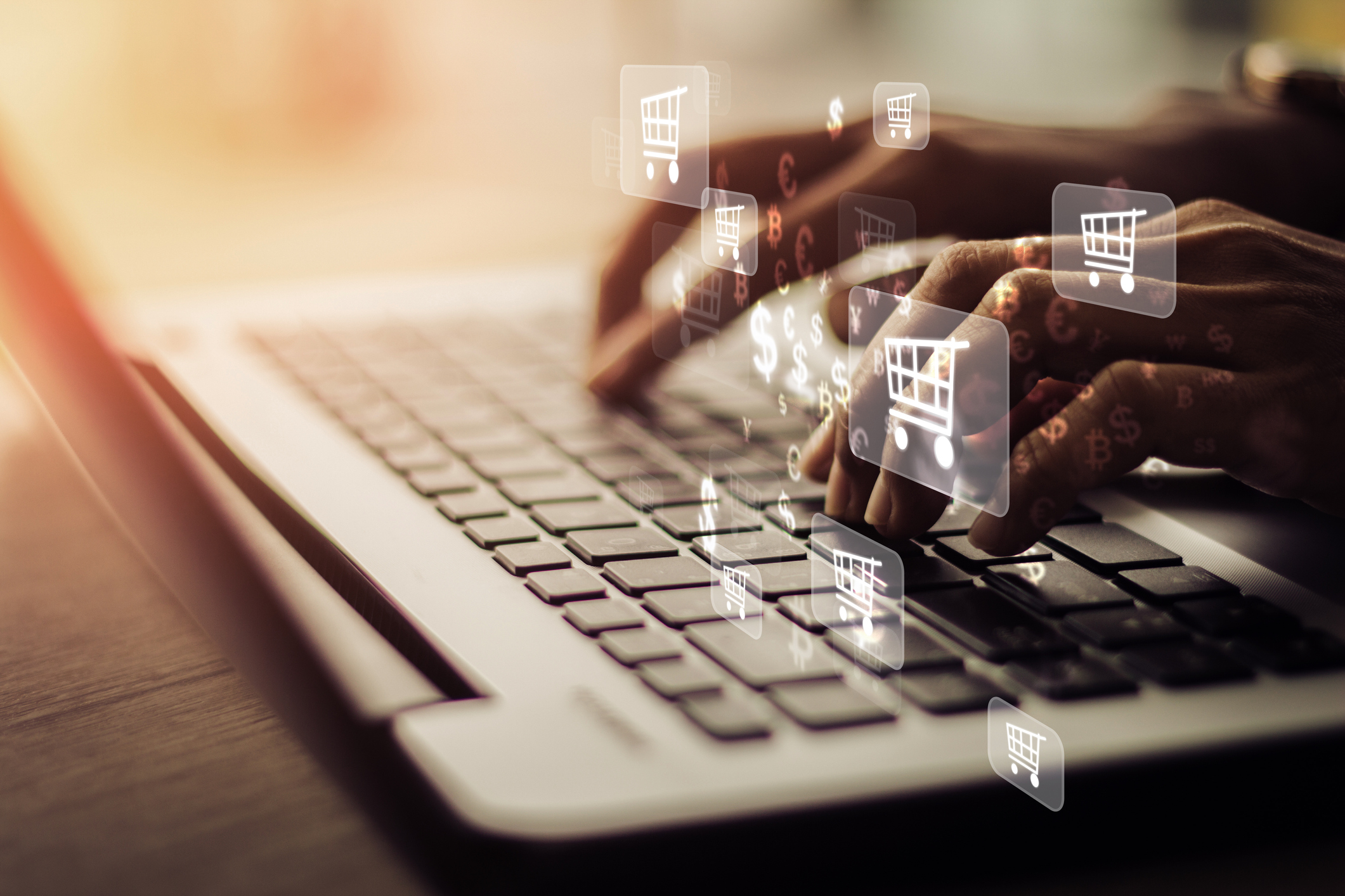 closeup of hands on a laptop keyboard with shopping cart icons flying around them.