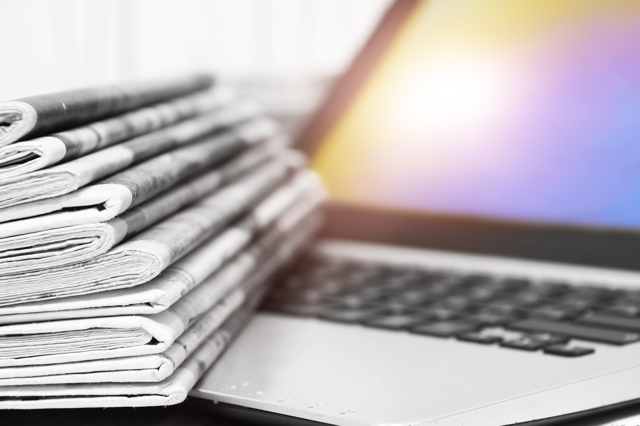 Stack of newspapers atop a laptop.
