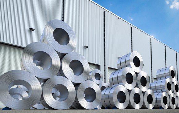Coils of aluminum sheet stacked outside a manufacturing warehouse.