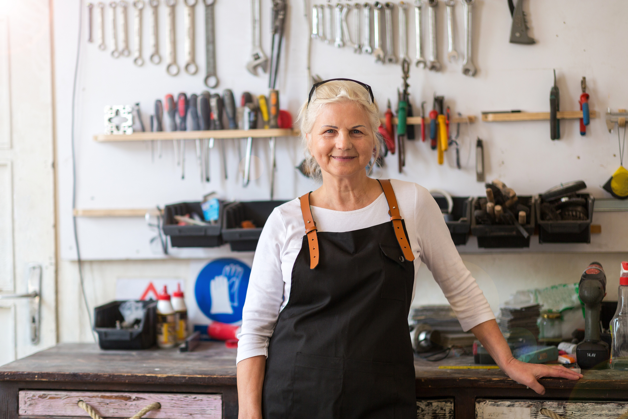 A senior woman standing in front of a bench in her workshop.