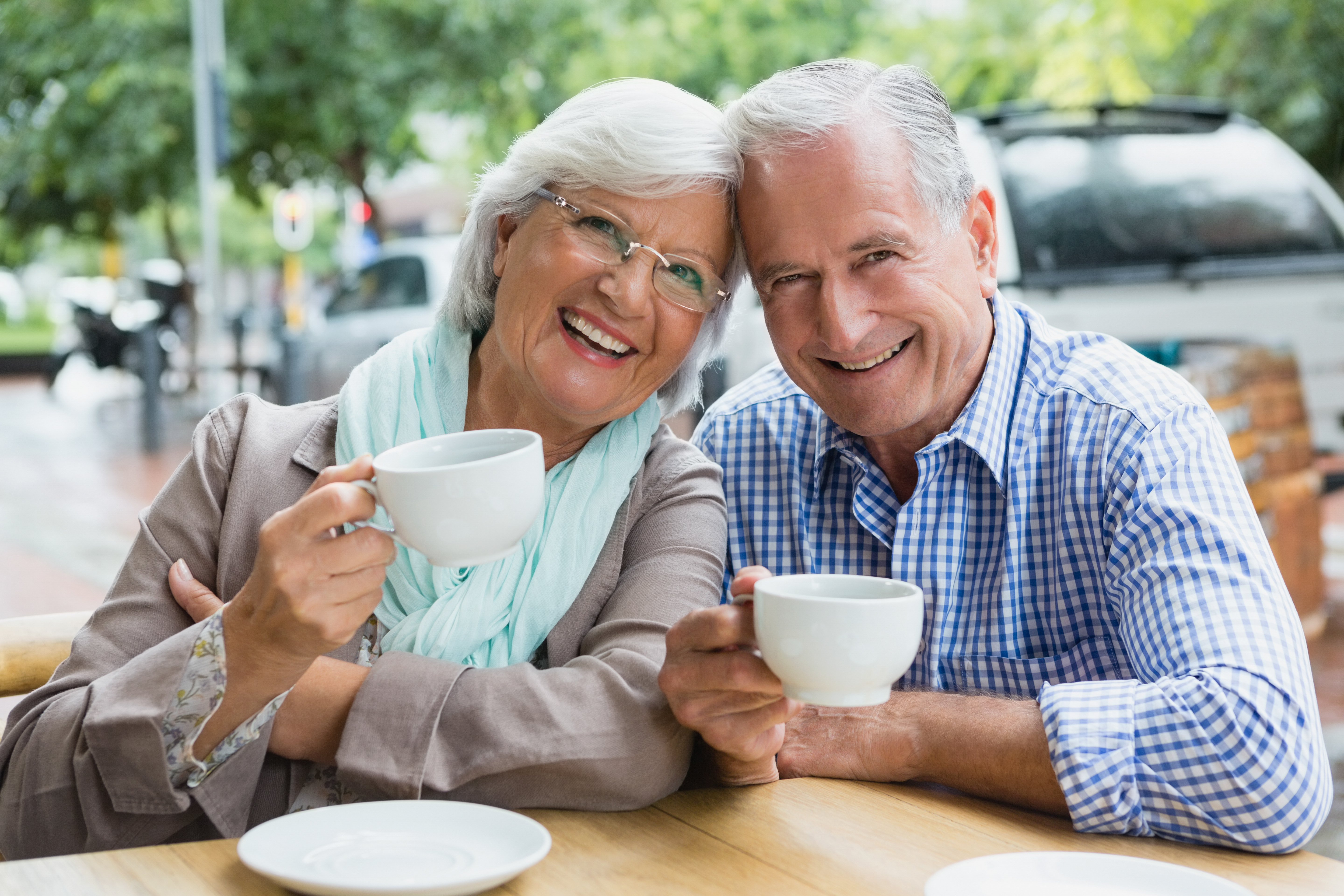 Smiling older man and woman holding mugs at a table outdoors