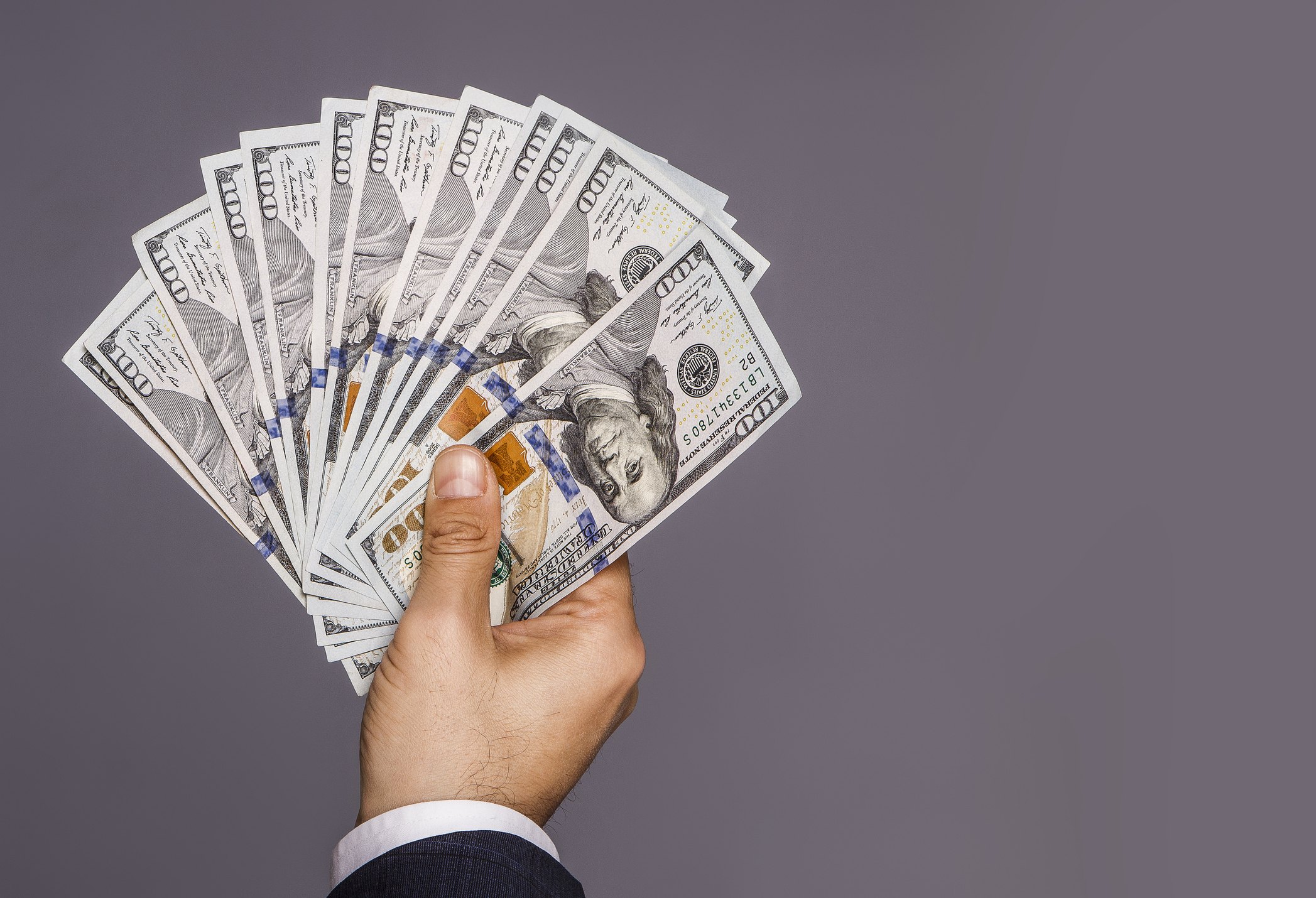 Man holding up hundred-dollar bills in the shape of a fan