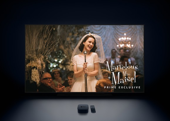 Apple TV set-top box next to remote in front of TV showing a still from "The Marvelous Mrs. Maisel"