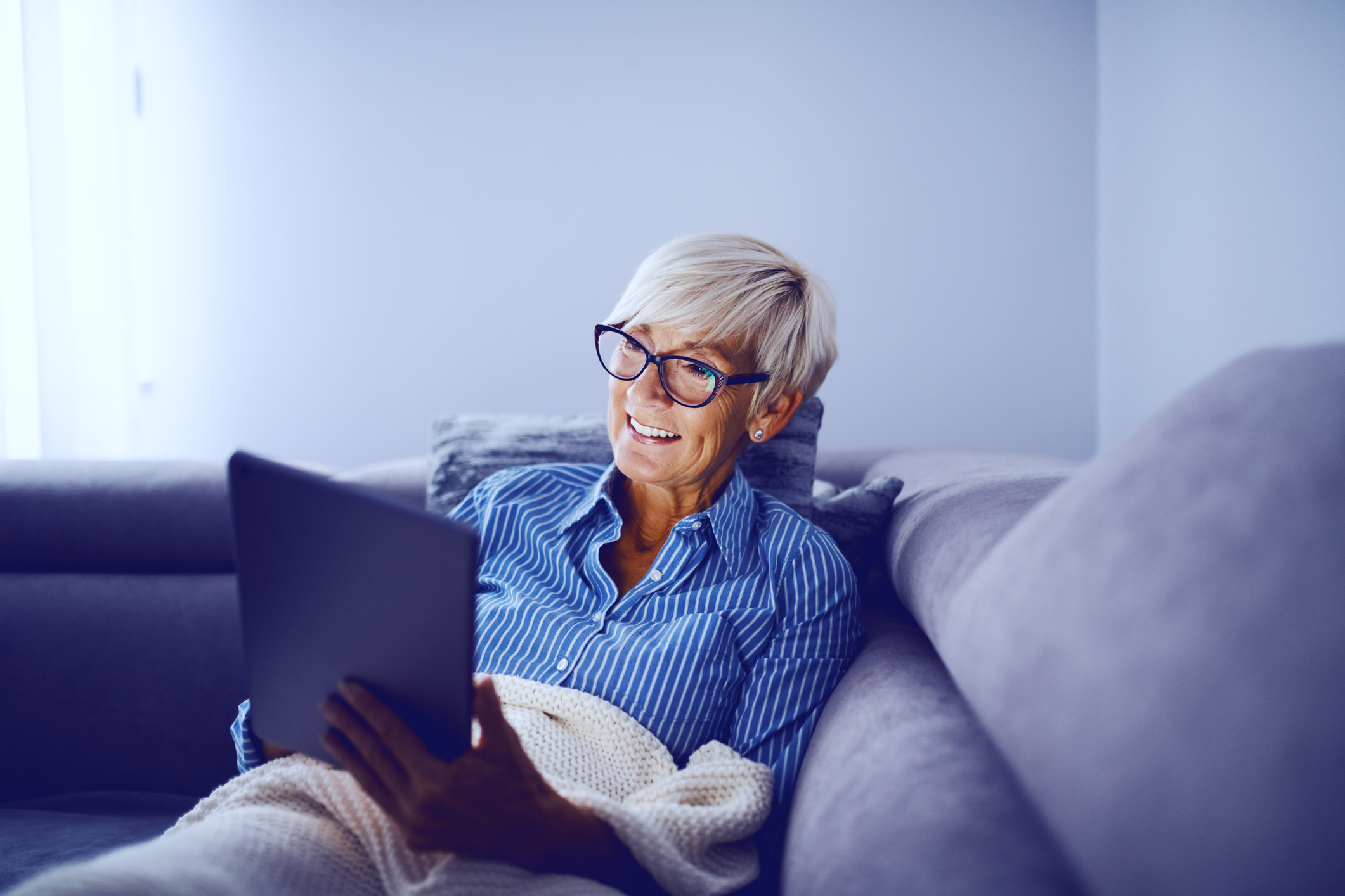 Smiling older woman holding tablet on couch