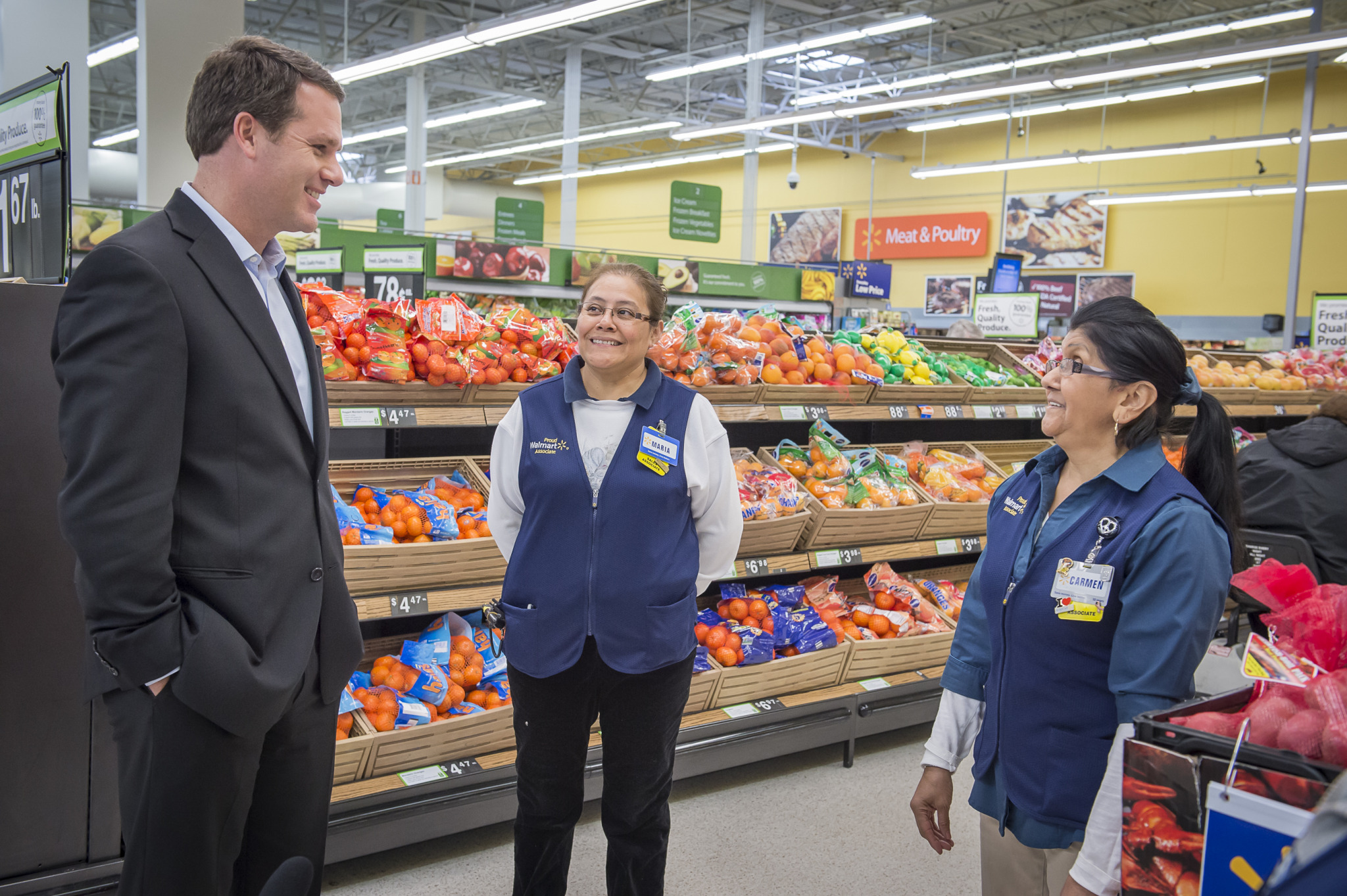CEO Doug McMillon talking with two associates in a Walmart store produce aisle.