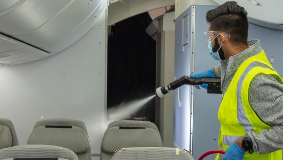 A person wearing a mask spraying aerosol disinfectant on a plane. 