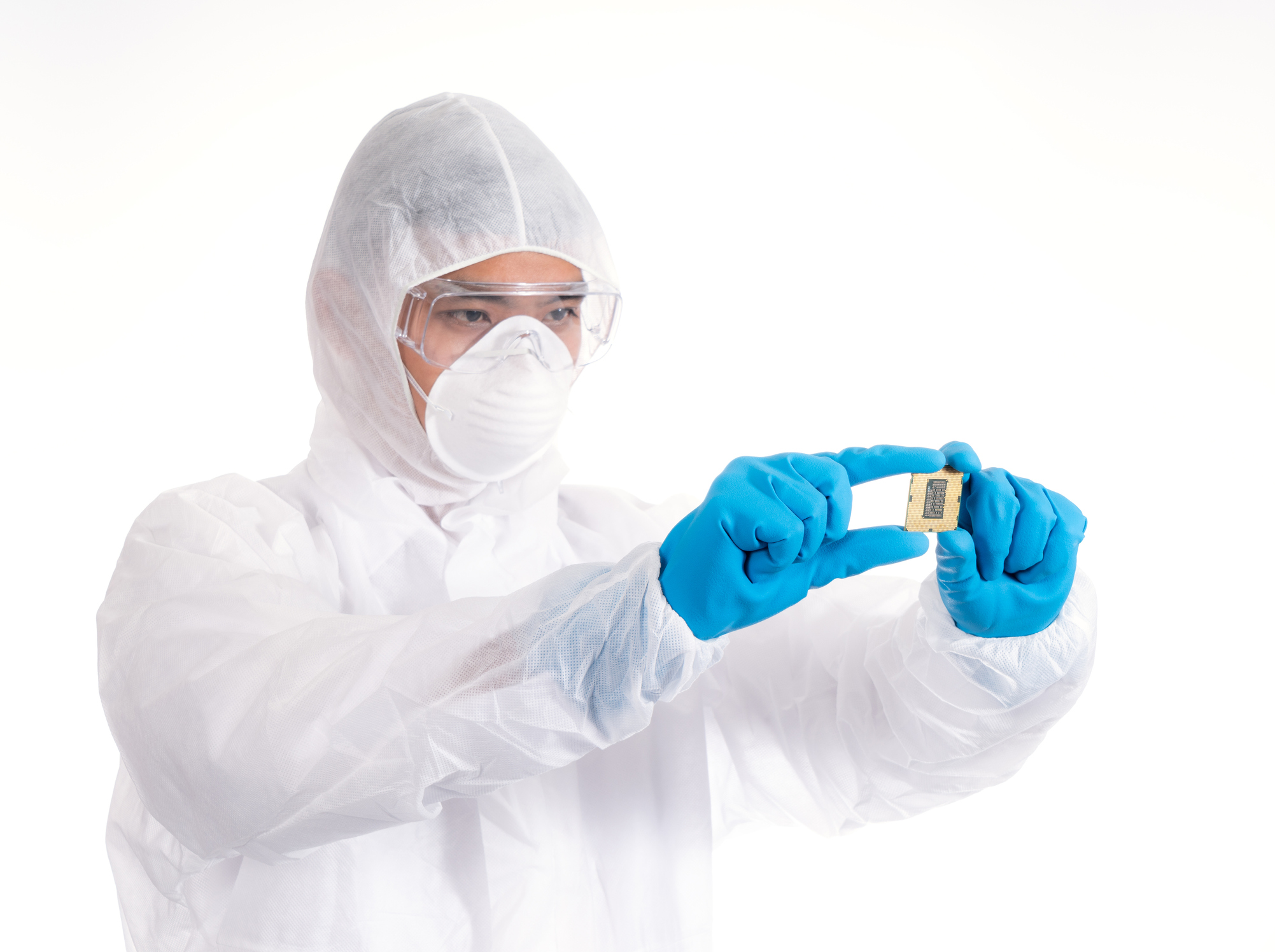 Engineer in protective suit, looking at a microchip as he holds it up.