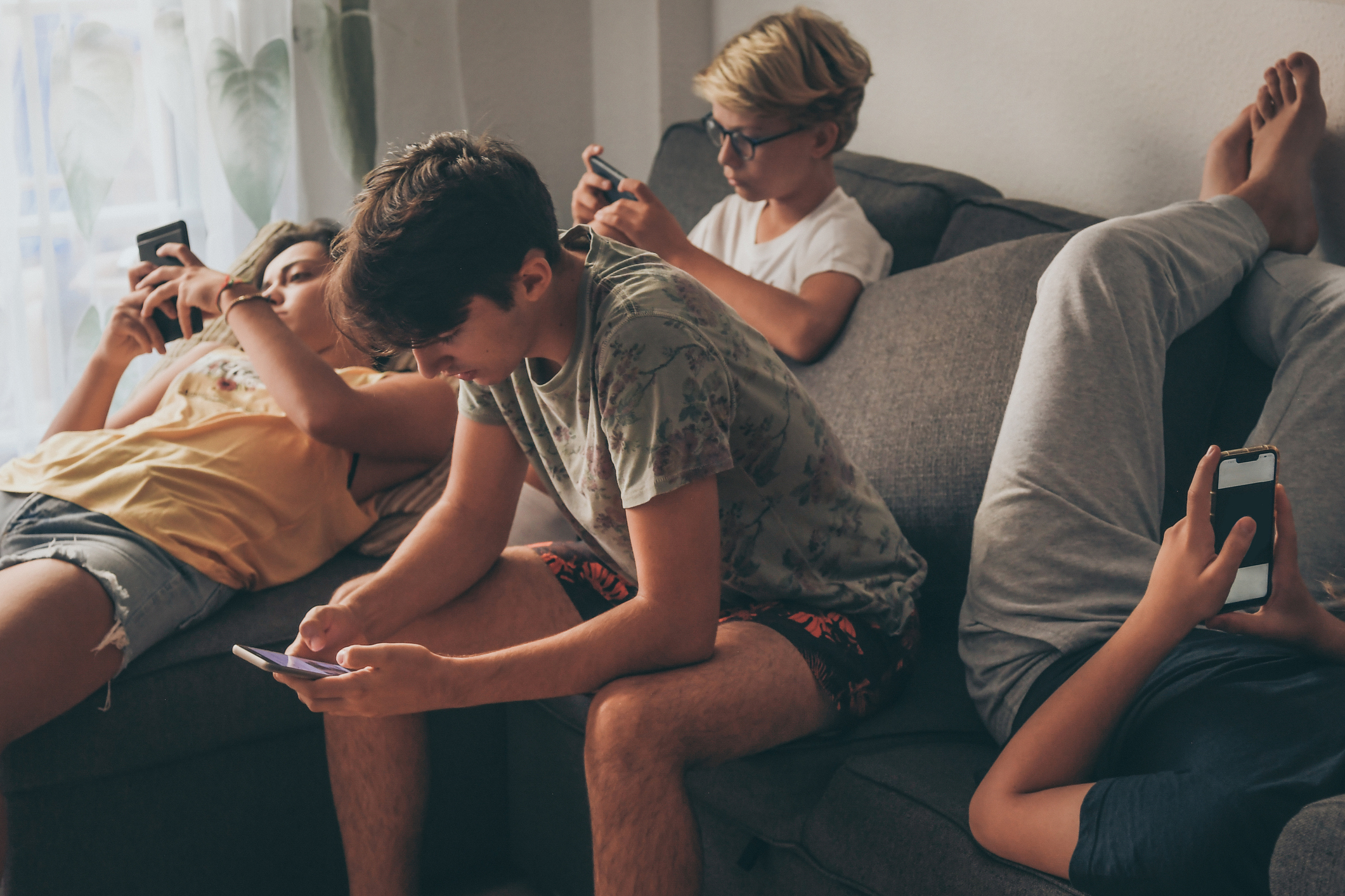 Teens sitting on a couch staring at their respective smartphones.