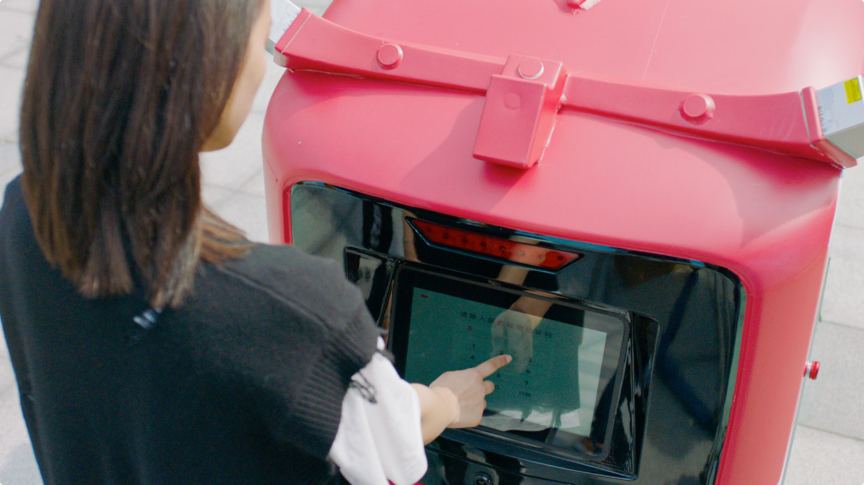 A woman presses a touch screen on a delivery robot.