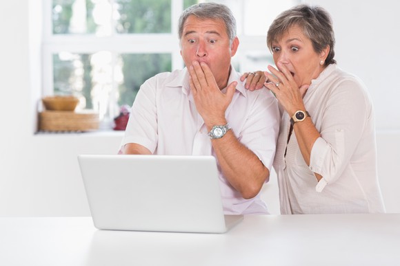 Older man and woman at laptop, covering their mouths as if in shock