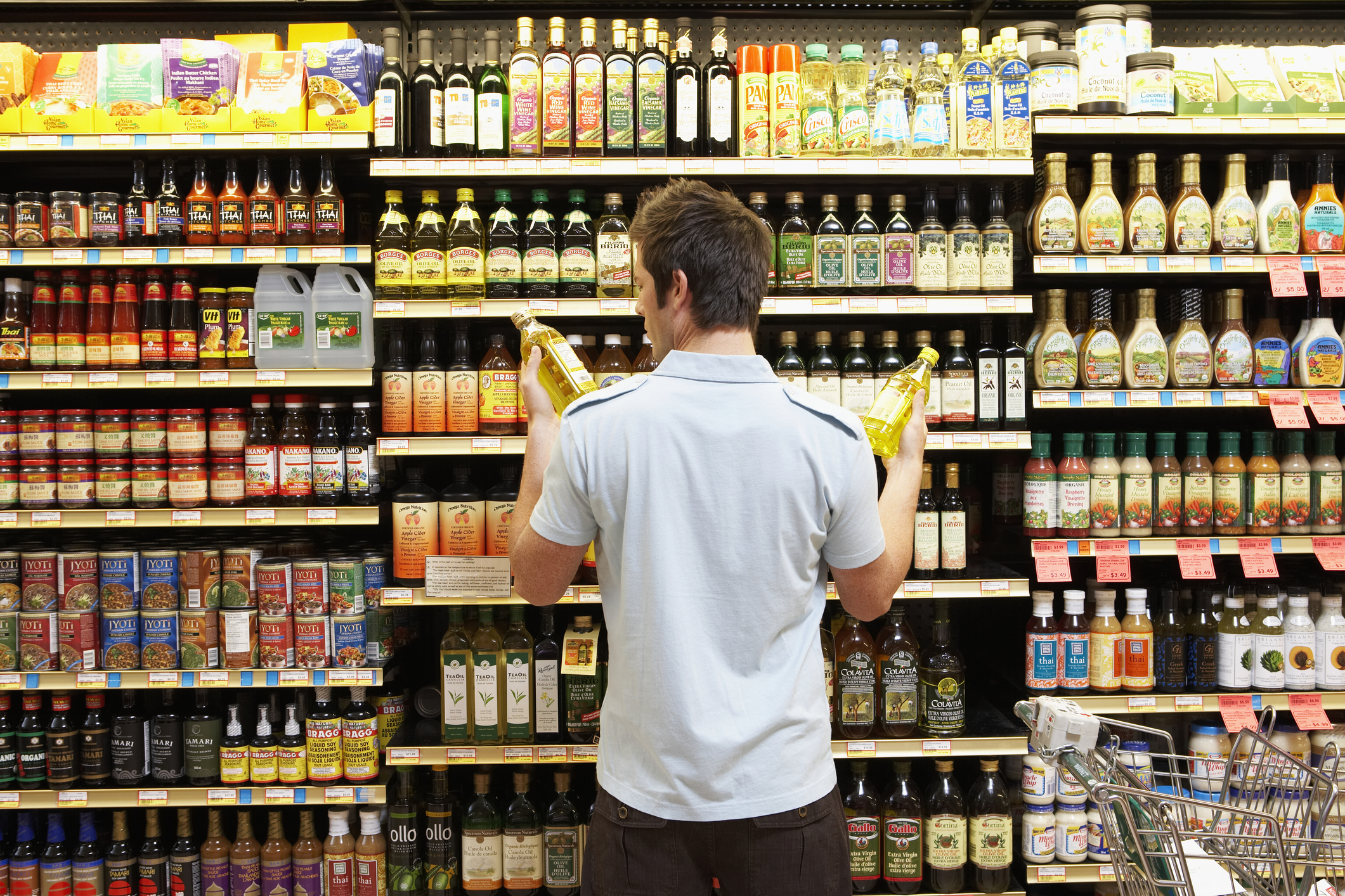 A man shopping the cooking oil section at a supermarket.