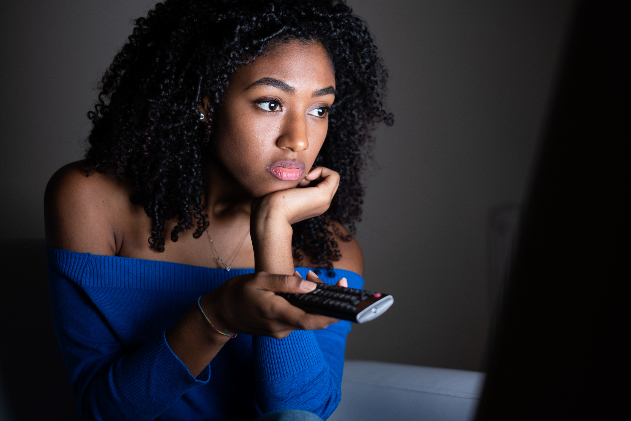 A young woman watches TV in a dim room.