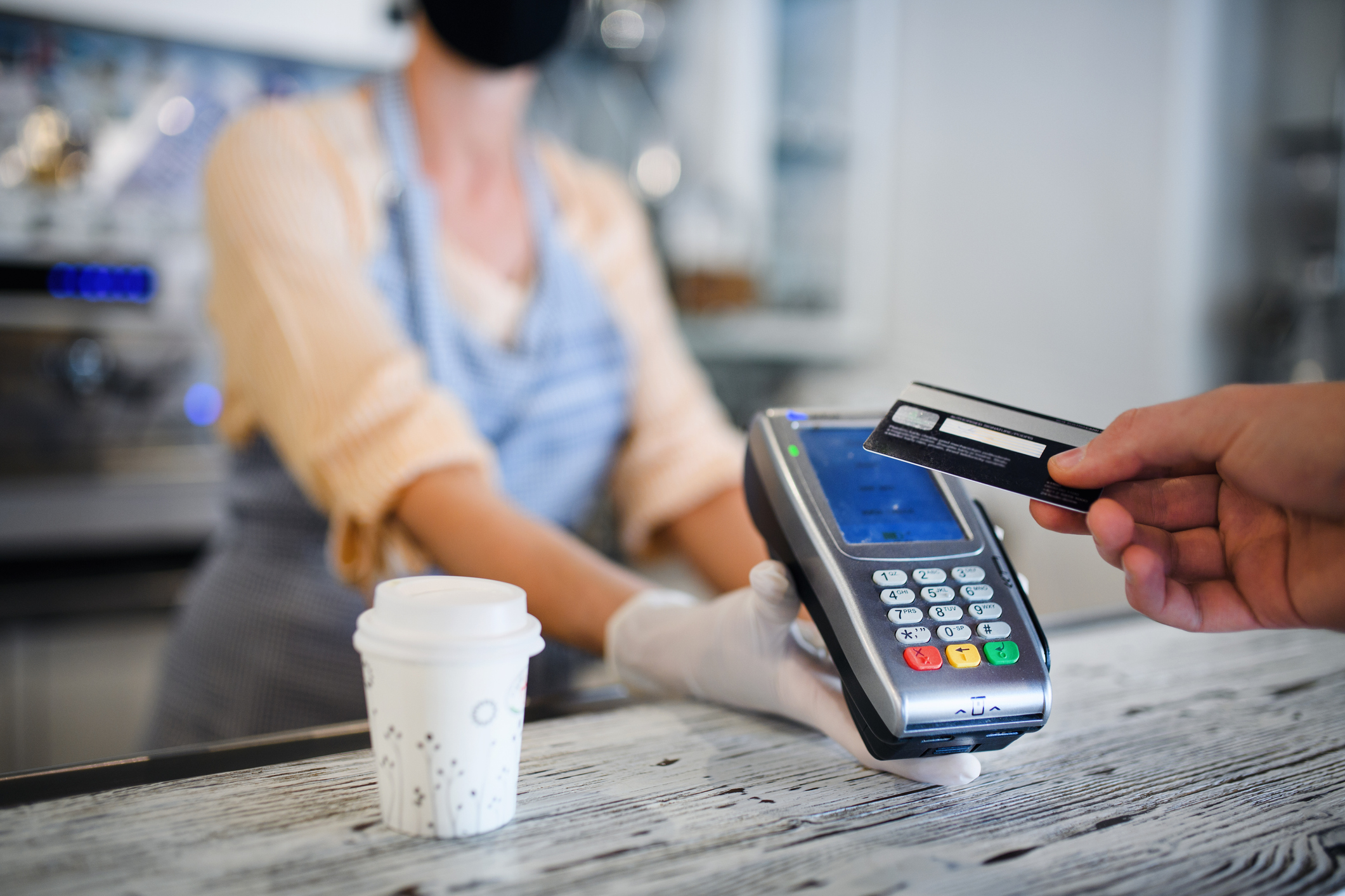 A merchant wearing a mask holds out card swiper for buyer using credit card