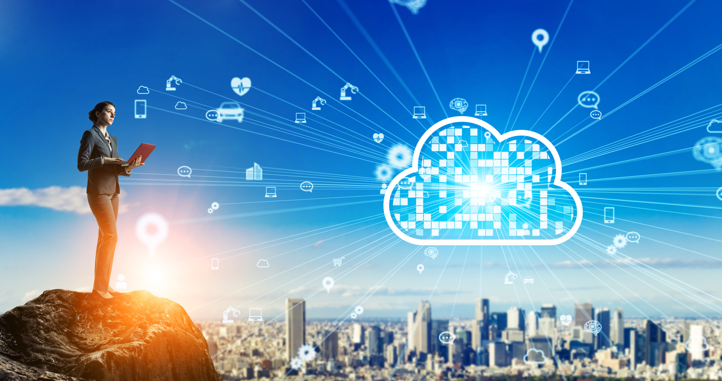 Woman standing on a mountain top above a city as she holds her laptop and connects to the cloud hovering above the city.