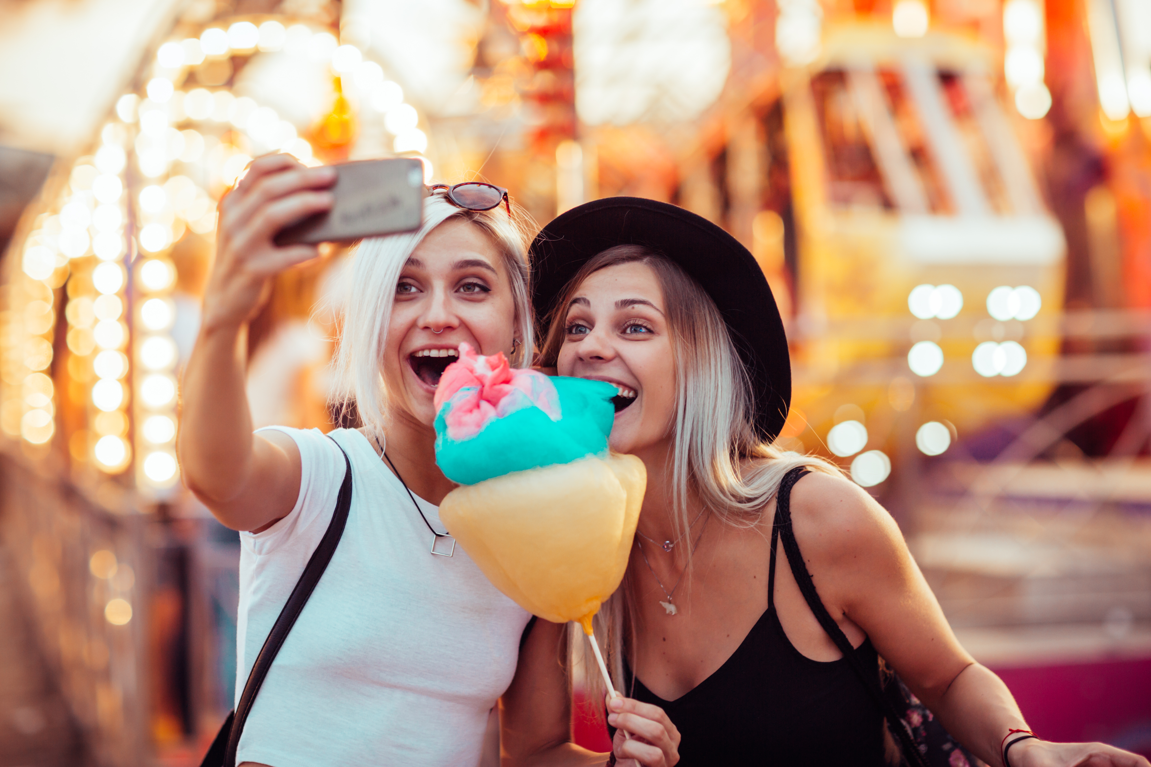Two women taking a selfie with cotton candy at a theme park.