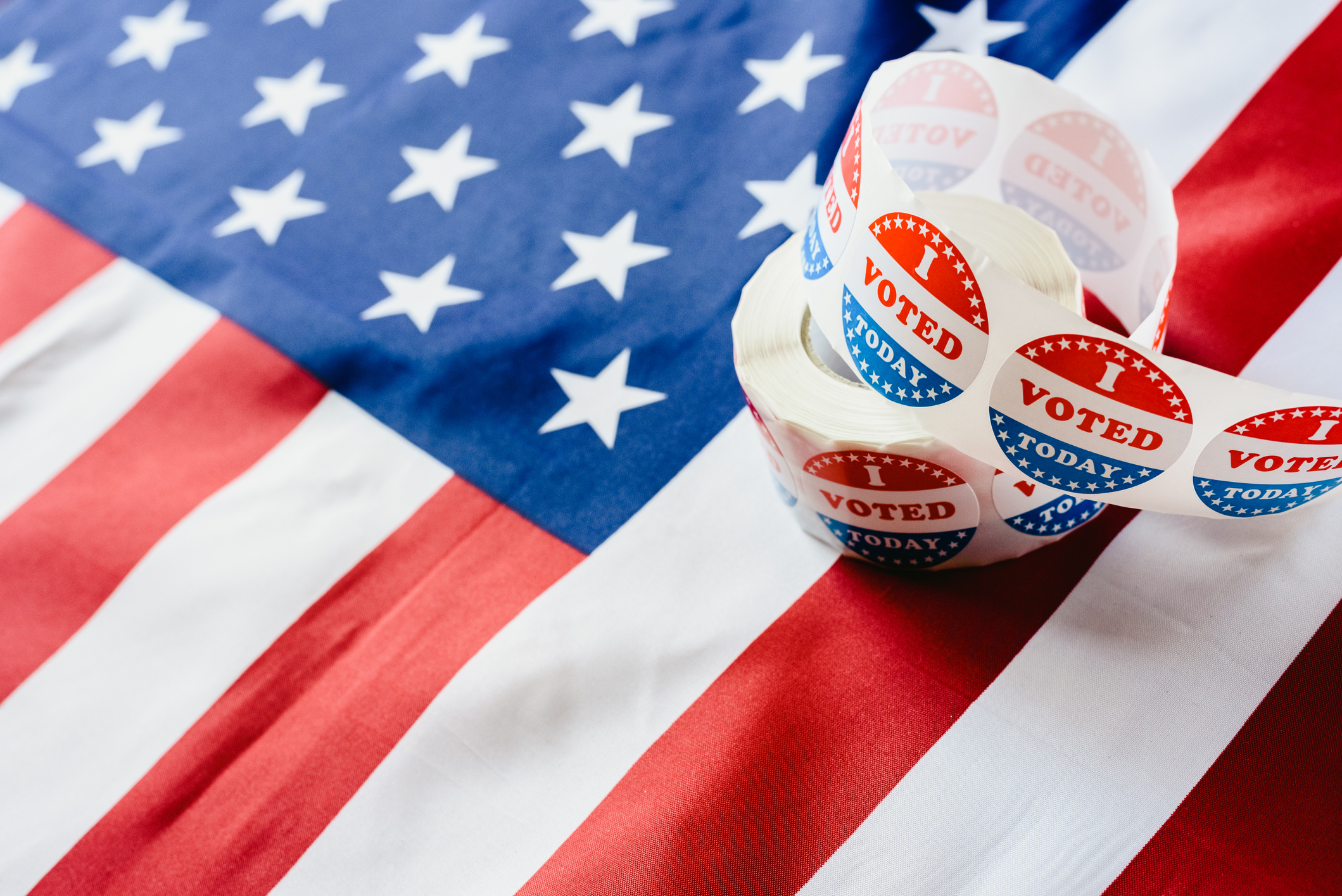 An American flag background with an I voted sticker roll on top of it.