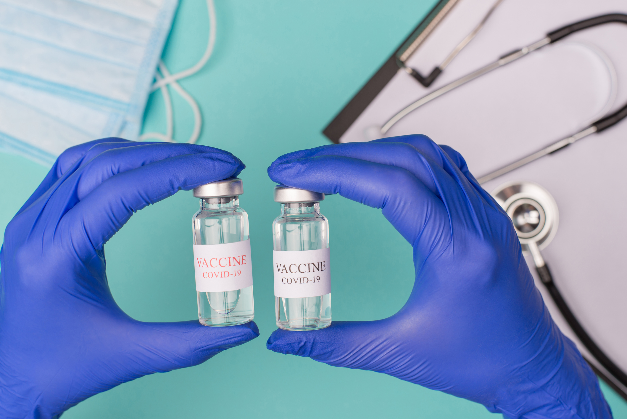 Gloved hands holding two COVID-19 vaccine bottles