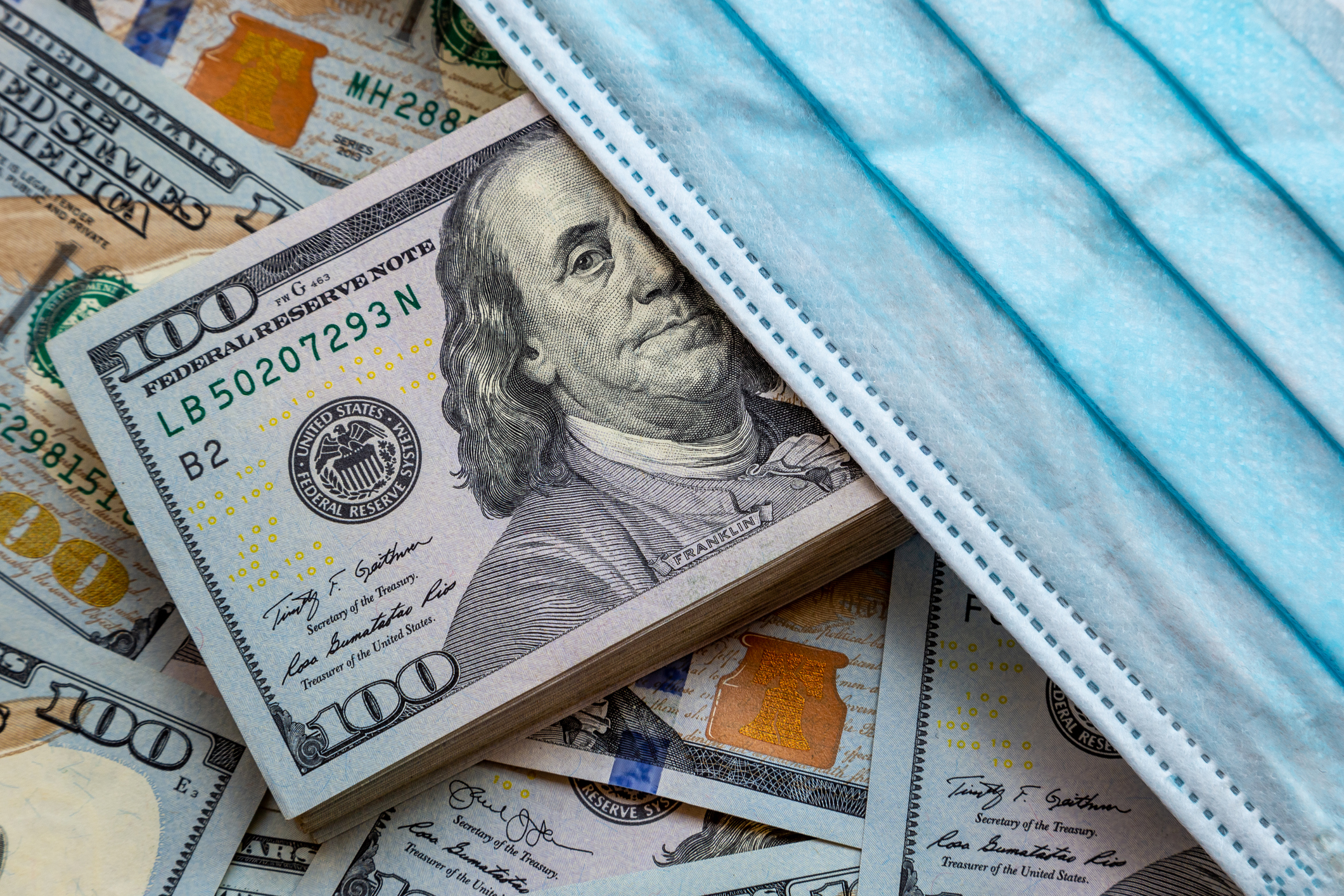 Hundred dollar bills laying on a surface with a coronavirus mask.