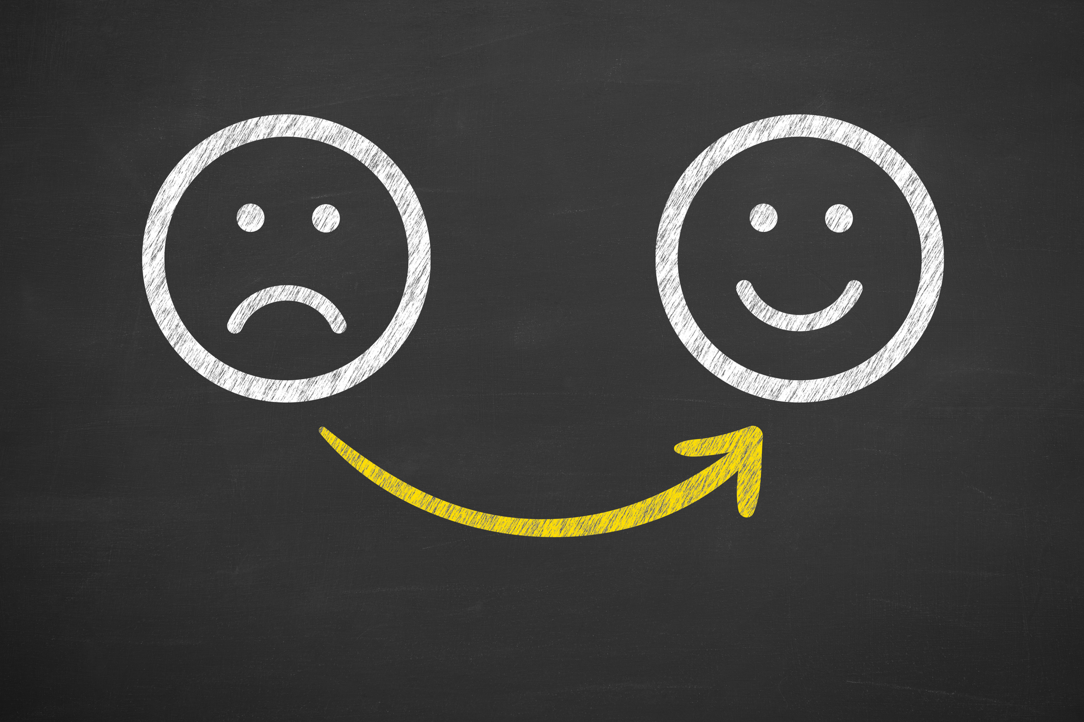 A sad face and a happy face drawn on a chalkboard.