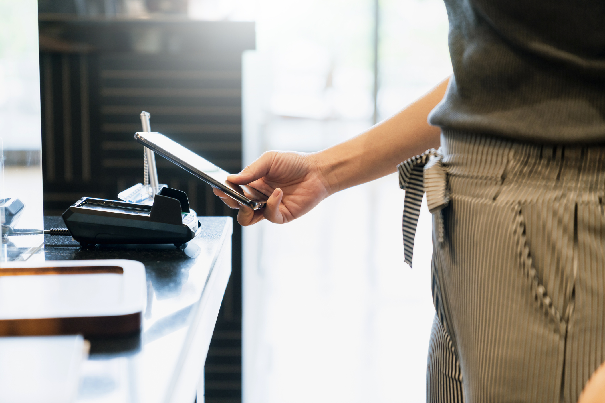 A person holding a smartphone near a touchless digital payment terminal.