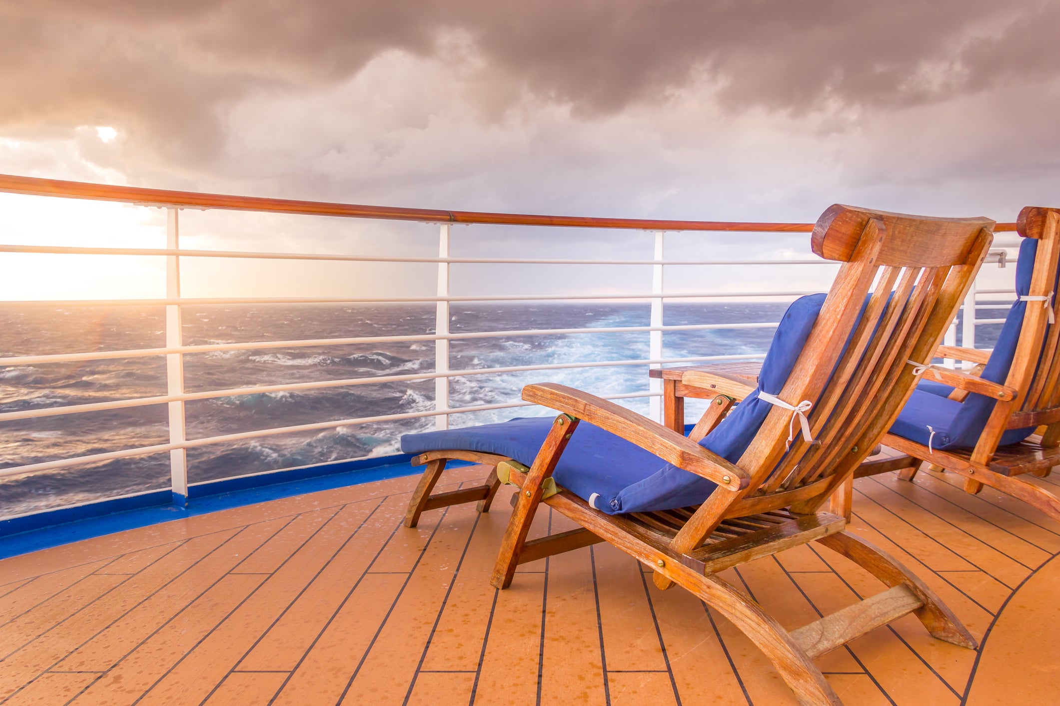 A pair of empty deck chairs overlooking the ocean water from a cruise ship.