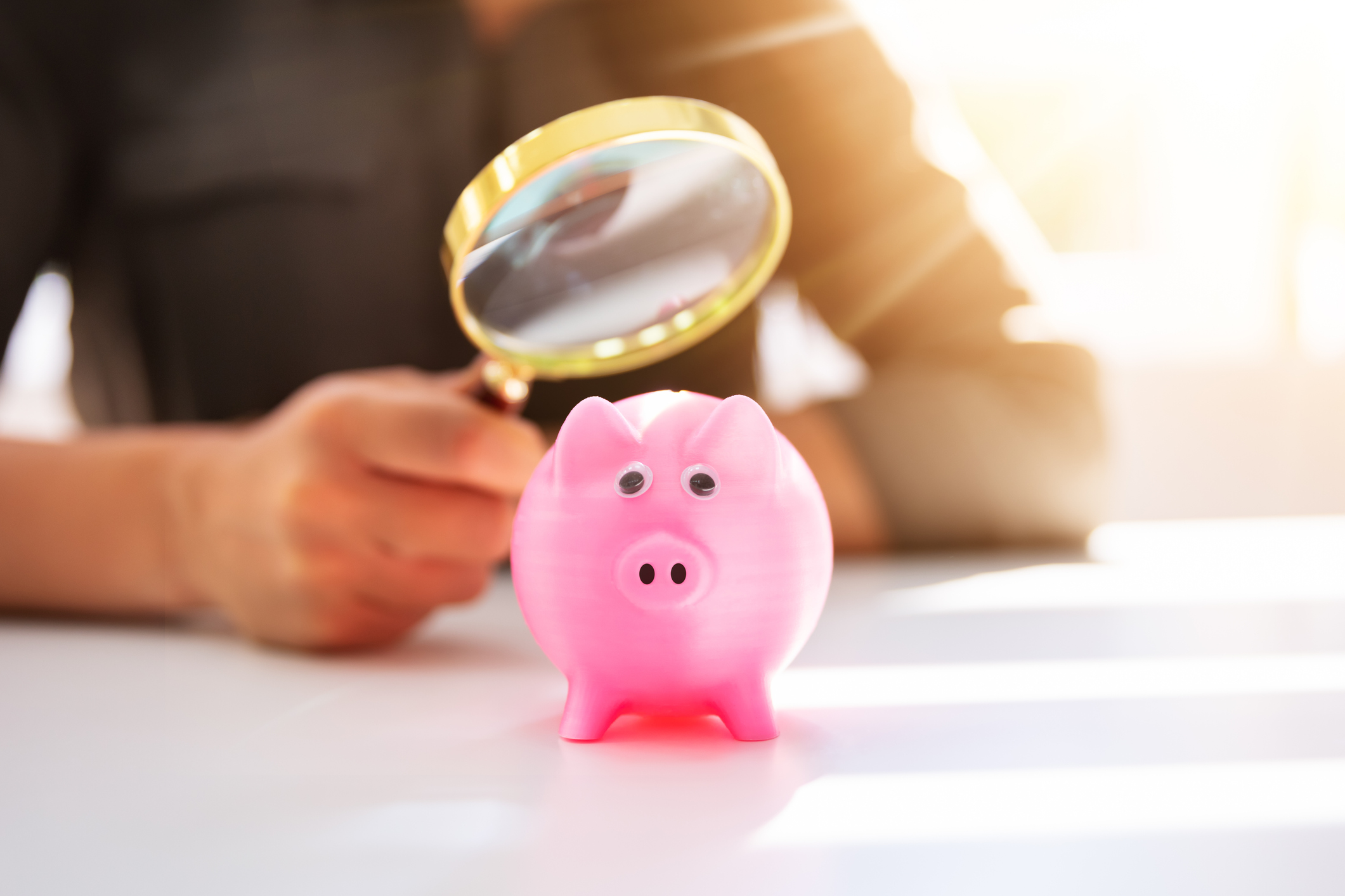 A businesswoman uses a magnifying glass to look at a pink piggy bank