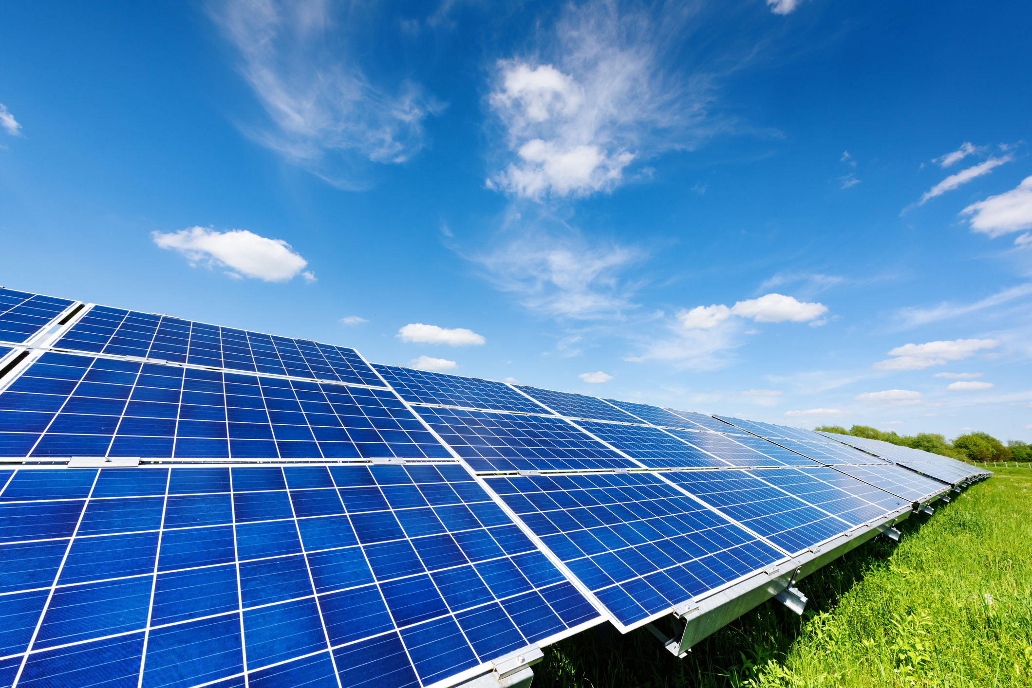 Solar panels in a green field with a bright blue sky.